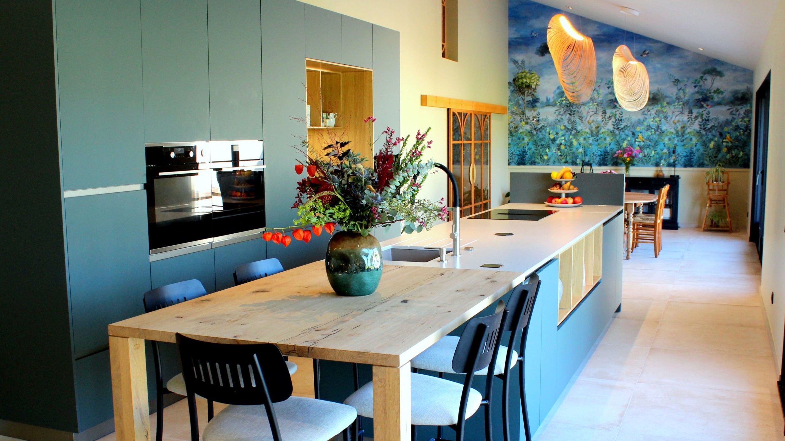 Vue d’ensemble d’une cuisine design avec façades vertes, îlot central en quartz et chêne massif, et mur panoramique végétal.