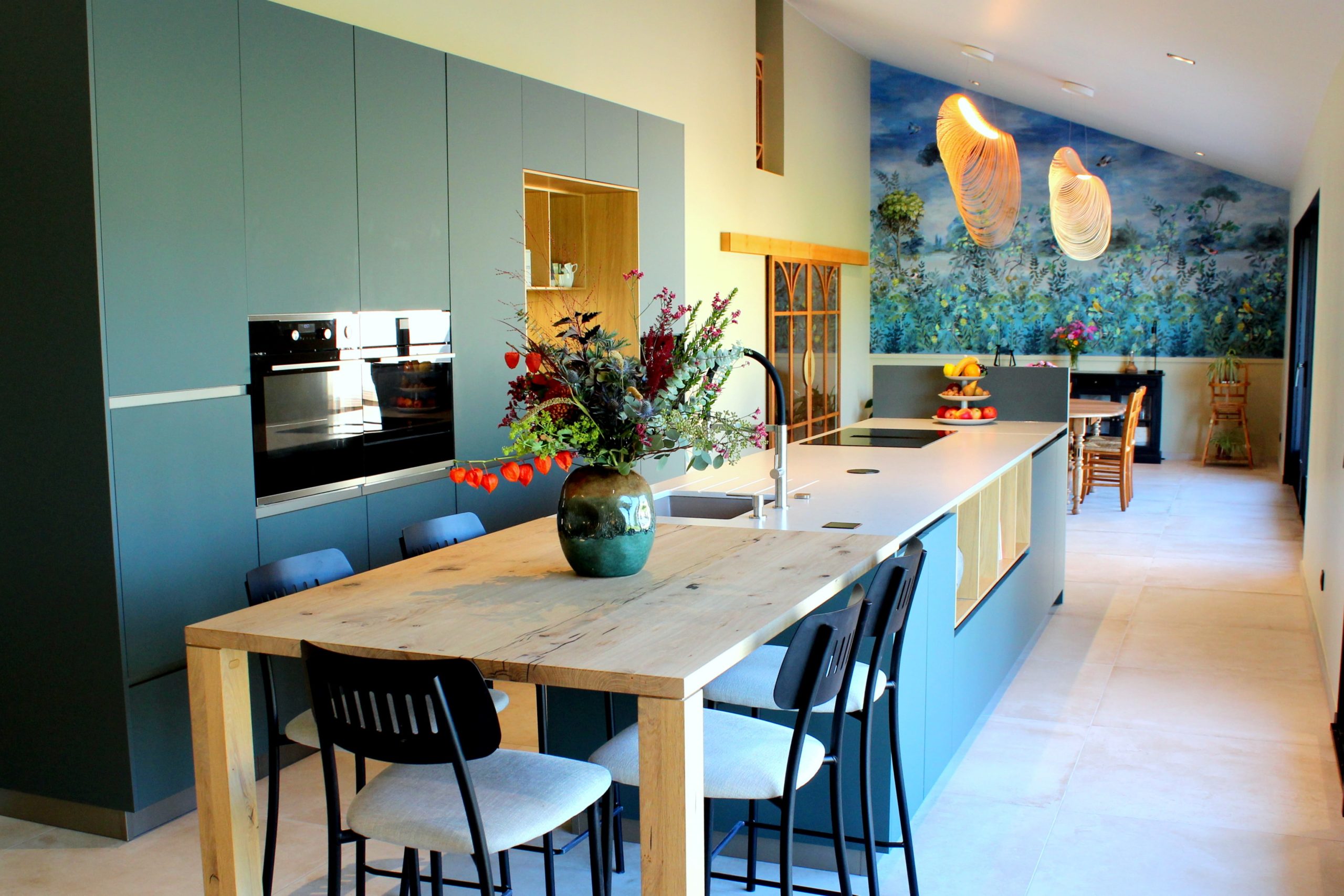 Vue d’ensemble d’une cuisine design avec façades vertes, îlot central en quartz et chêne massif, et mur panoramique végétal.