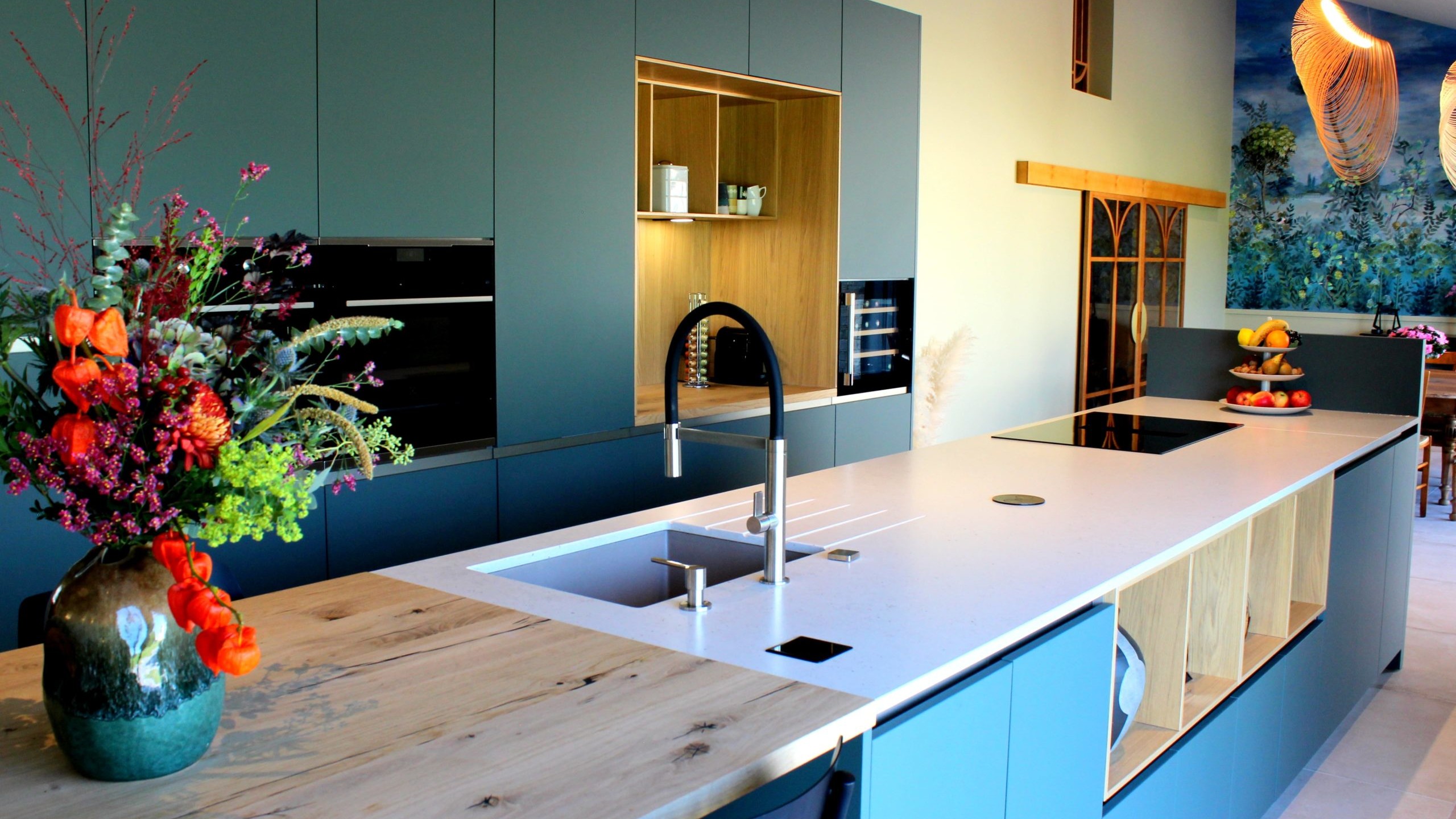 Vue d’ensemble d’une cuisine design avec façades vertes, îlot central en quartz et chêne massif, et mur panoramique végétal.