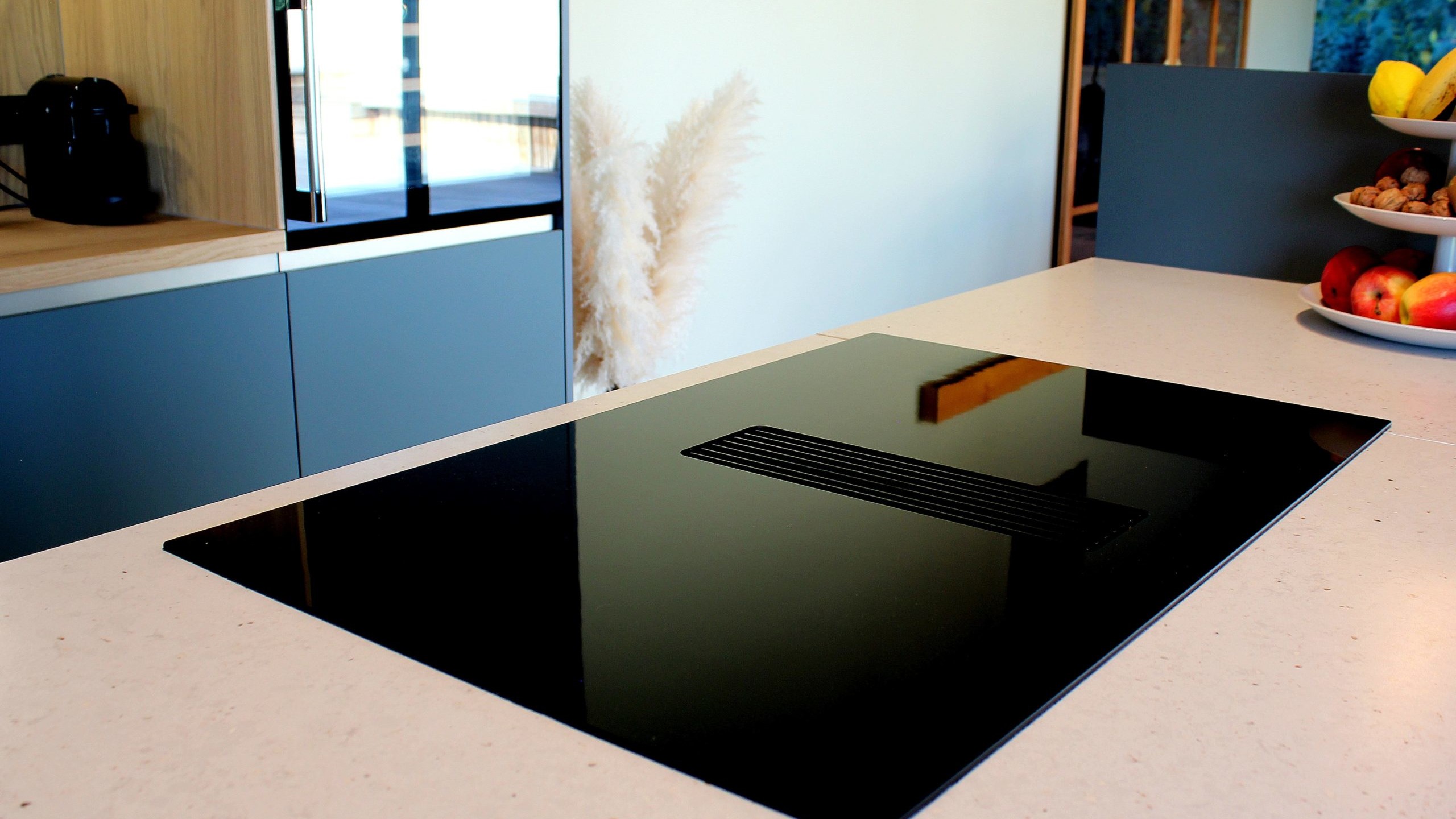 Vue d’ensemble d’une cuisine design avec façades vertes, îlot central en quartz et chêne massif, et mur panoramique végétal.