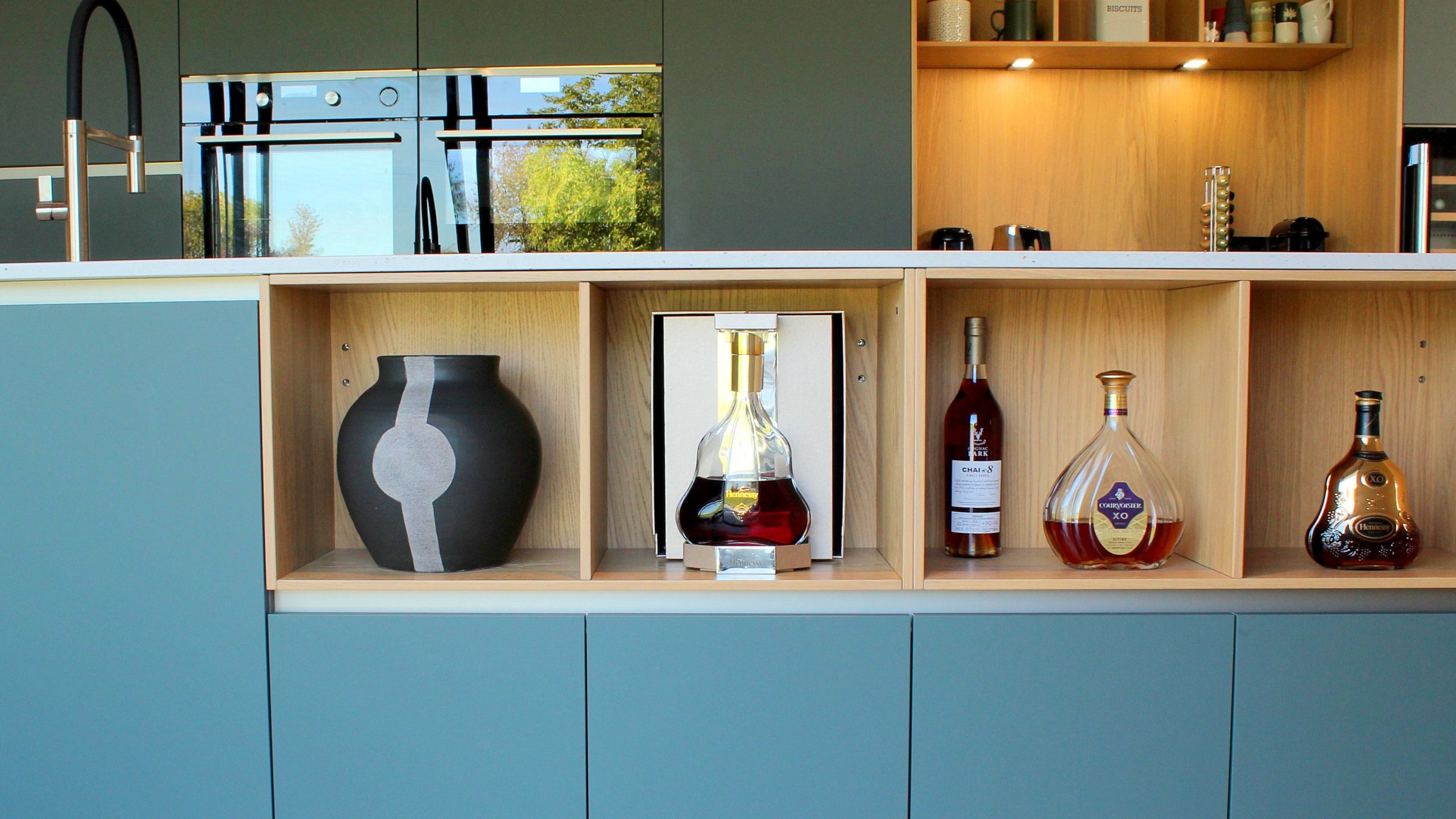 Vue d’ensemble d’une cuisine design avec façades vertes, îlot central en quartz et chêne massif, et mur panoramique végétal.