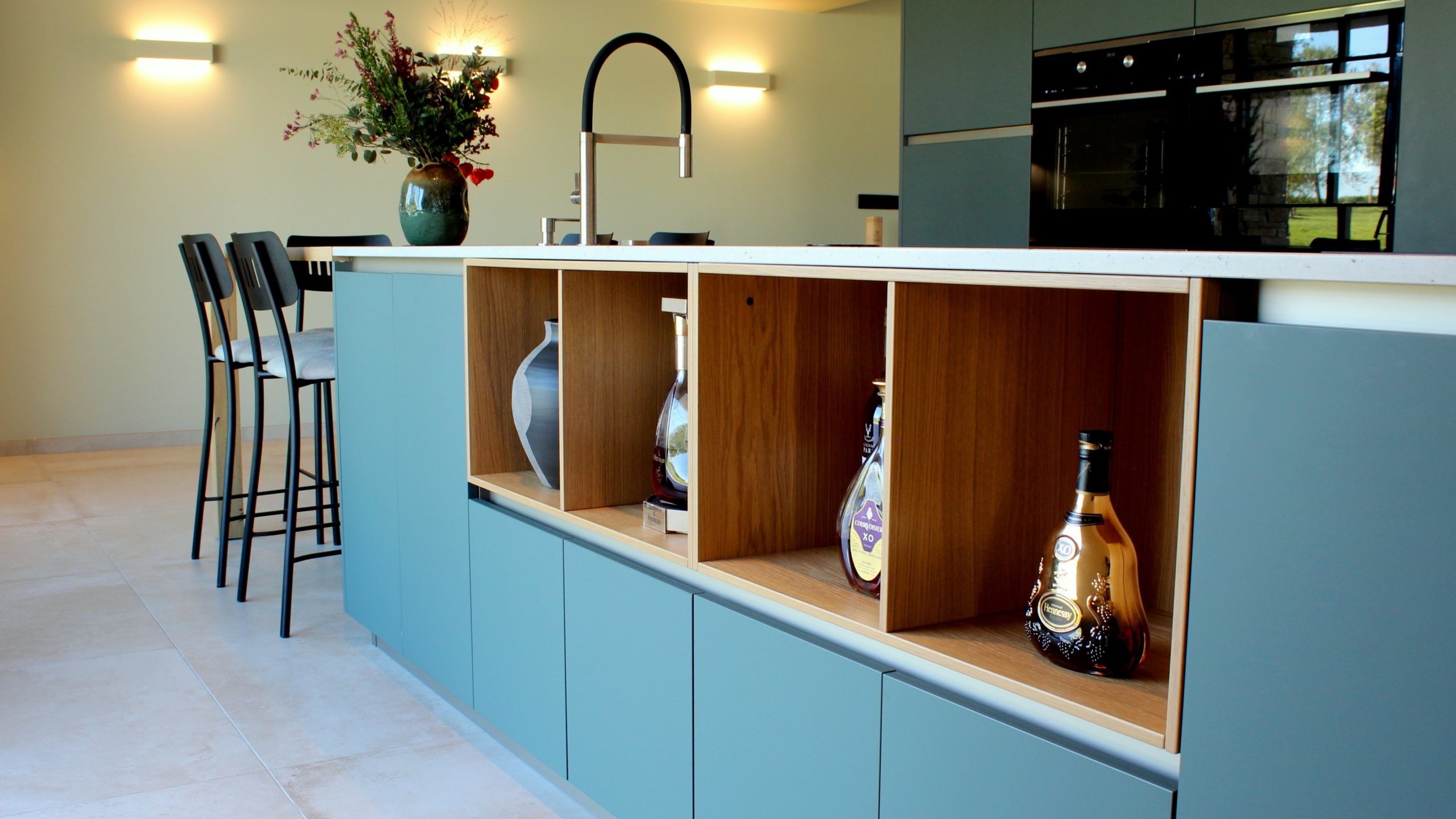 Vue d’ensemble d’une cuisine design avec façades vertes, îlot central en quartz et chêne massif, et mur panoramique végétal.