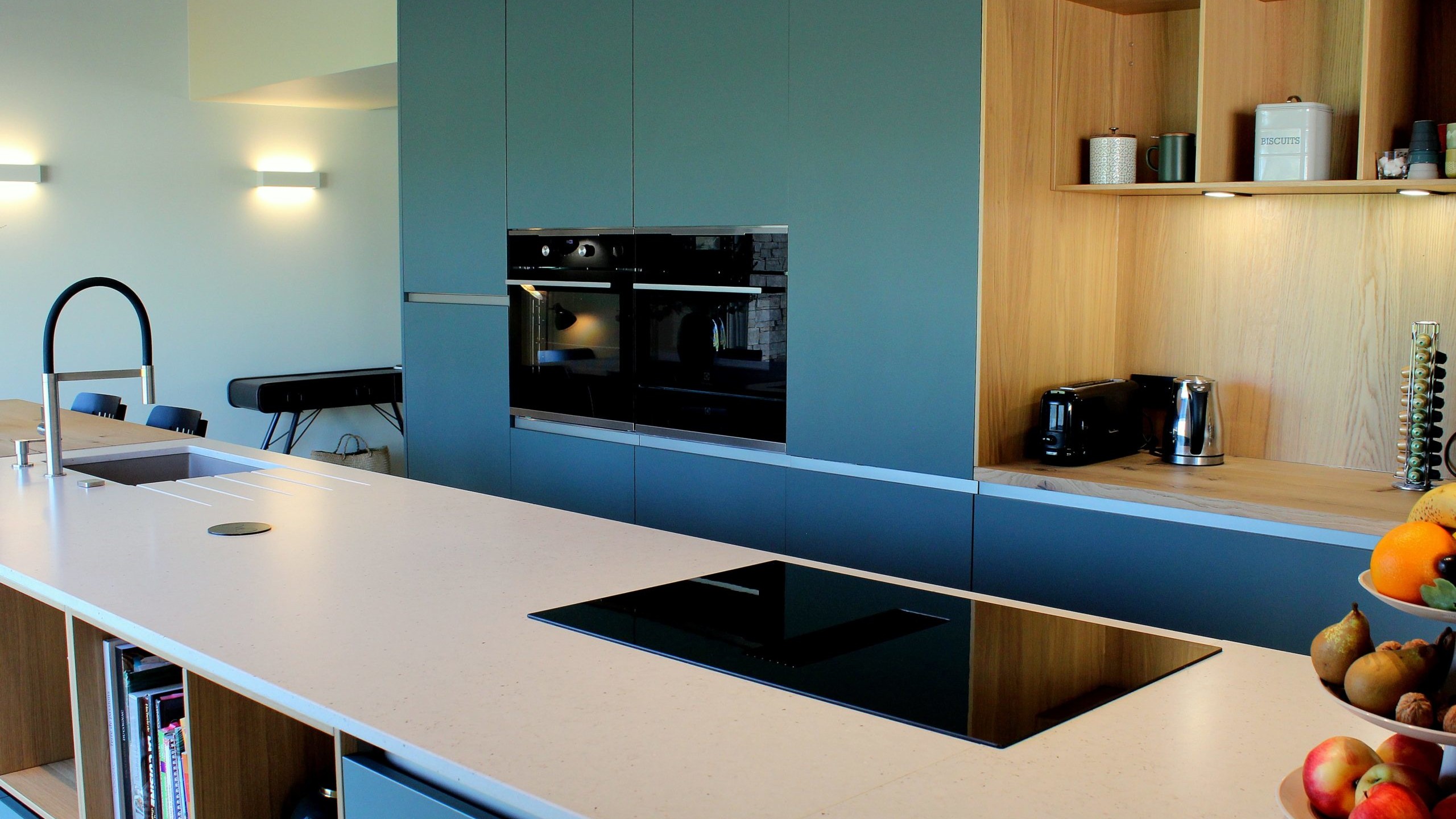 Vue d’ensemble d’une cuisine design avec façades vertes, îlot central en quartz et chêne massif, et mur panoramique végétal.