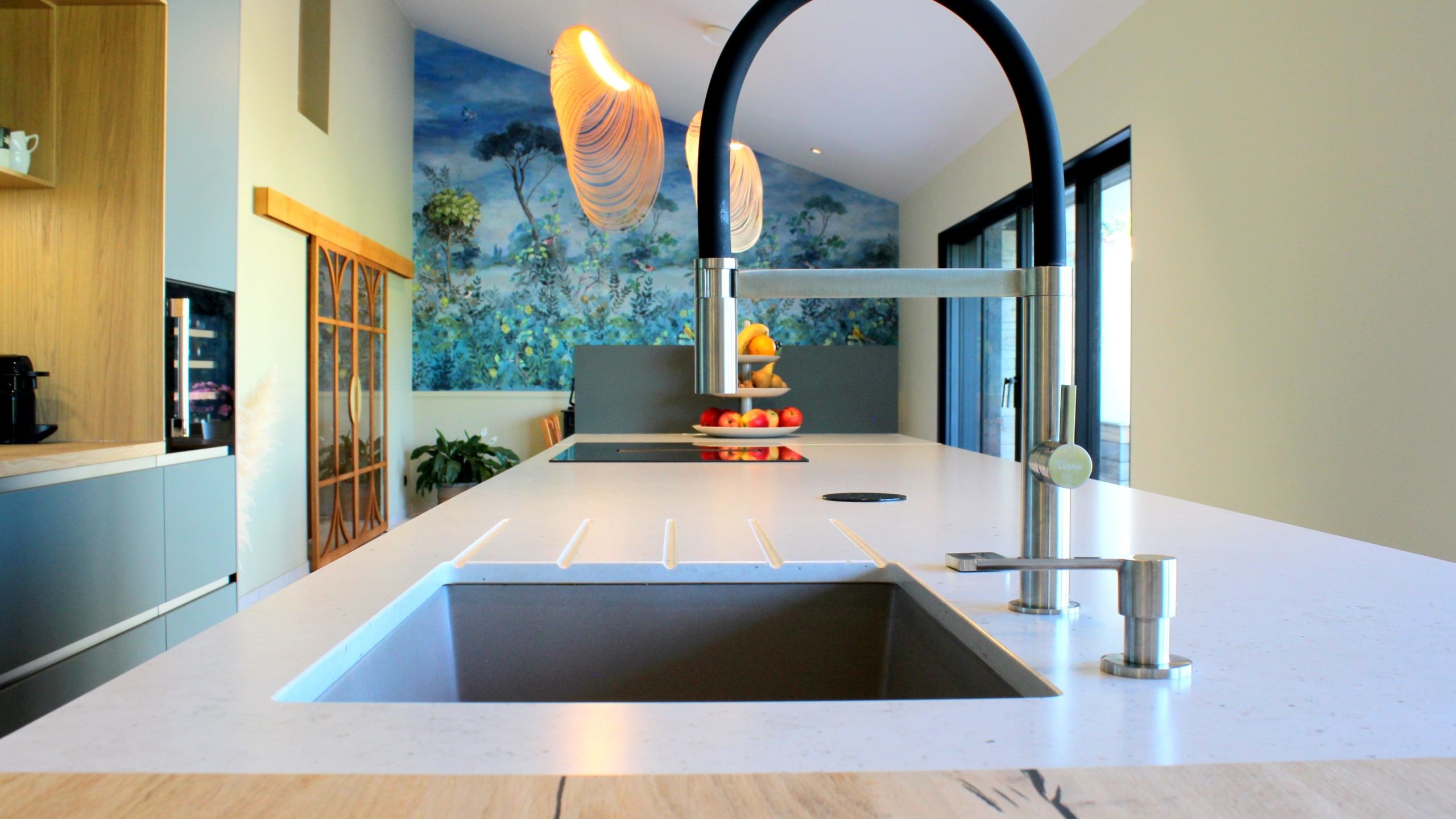 Vue d’ensemble d’une cuisine design avec façades vertes, îlot central en quartz et chêne massif, et mur panoramique végétal.