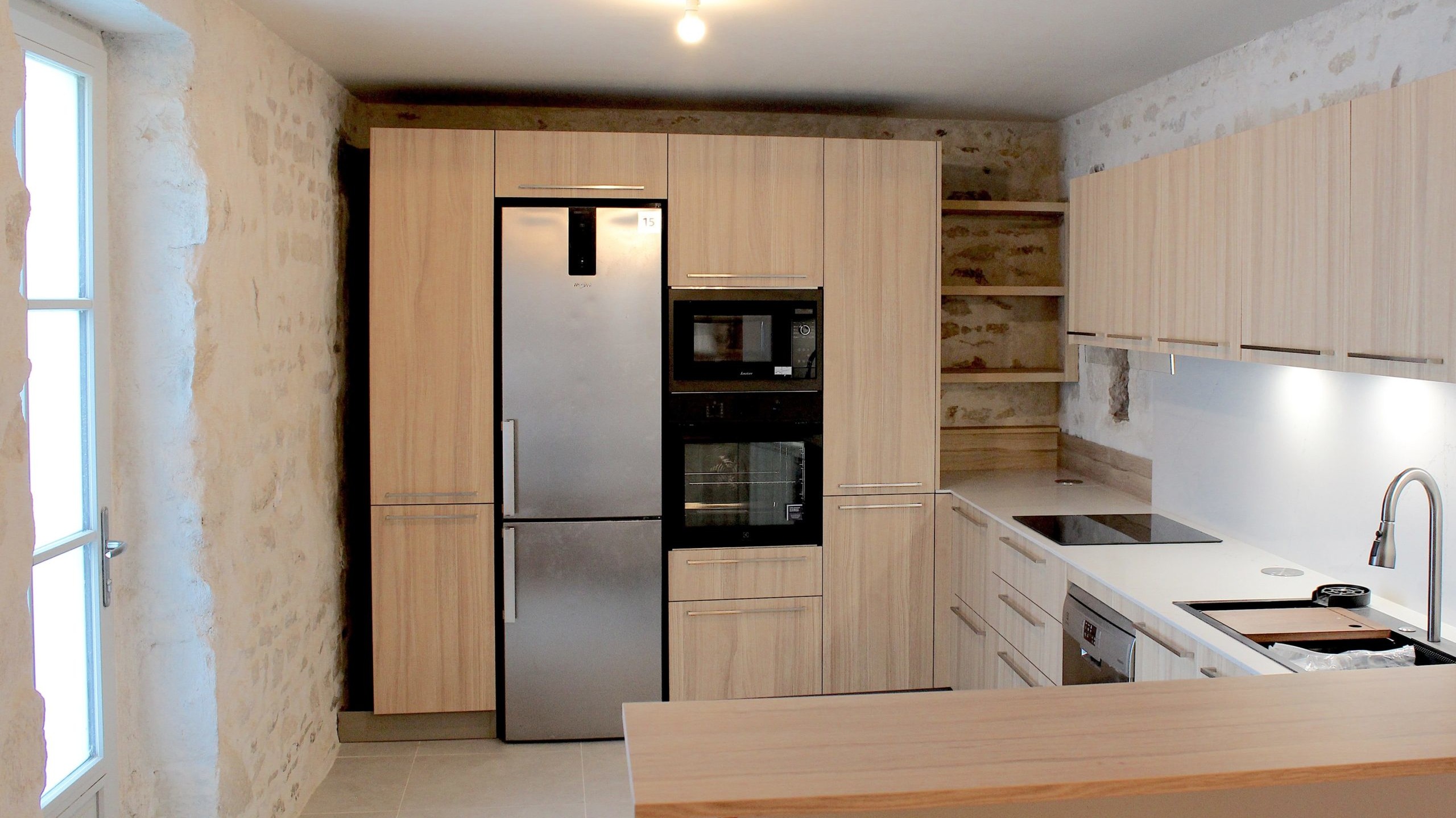 Cuisine moderne en placage bois clair avec plan de travail en quartz blanc, intégrée dans un intérieur en pierre à Nanteuil-en-Vallée.