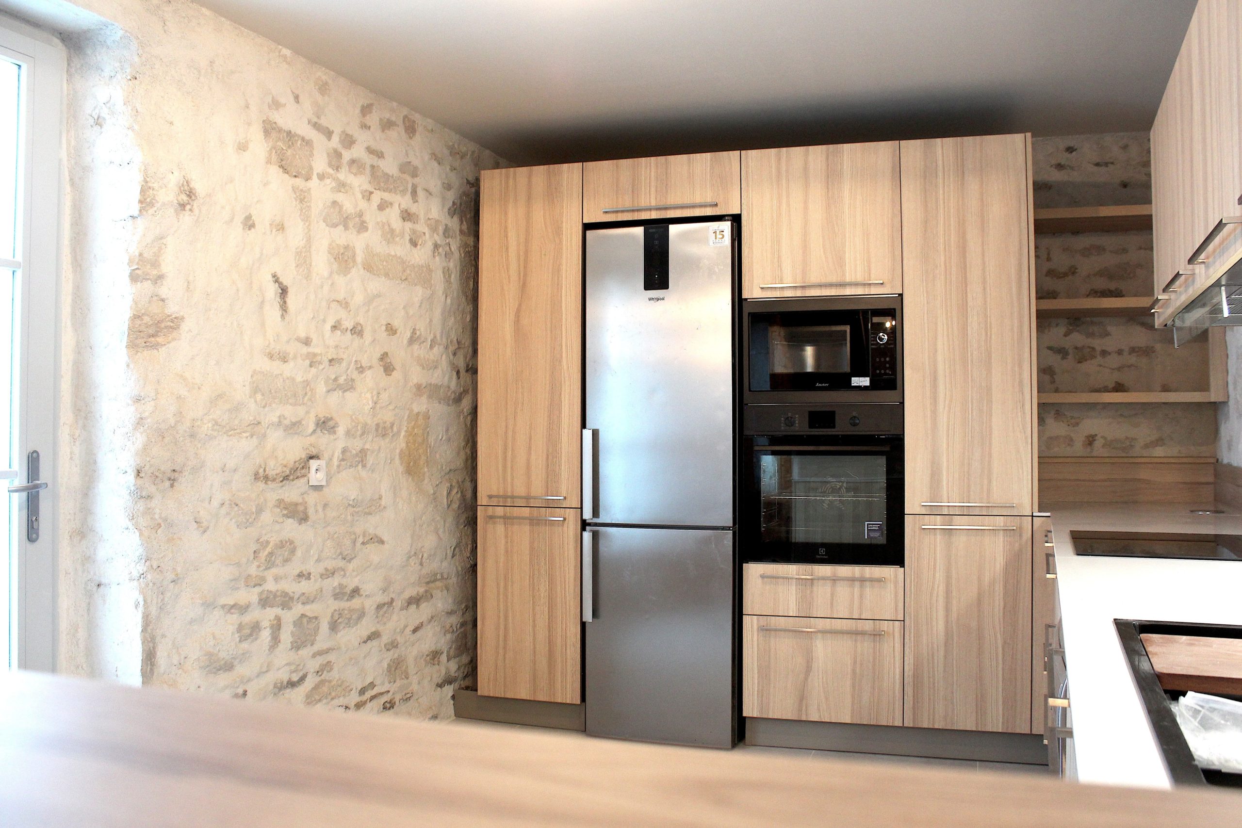 Cuisine moderne en placage bois clair avec plan de travail en quartz blanc, intégrée dans un intérieur en pierre à Nanteuil-en-Vallée.