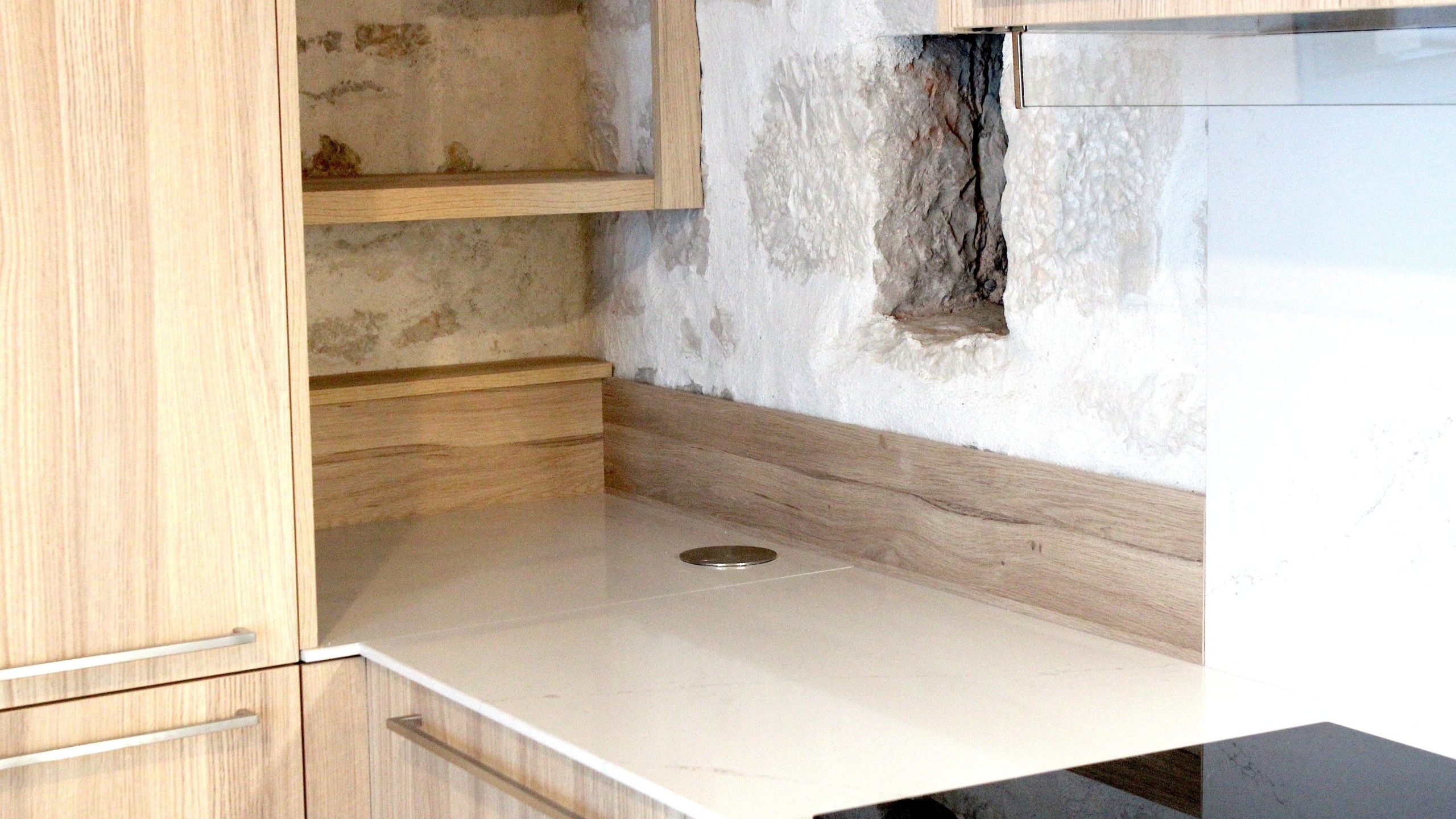 Cuisine moderne en placage bois clair avec plan de travail en quartz blanc, intégrée dans un intérieur en pierre à Nanteuil-en-Vallée.