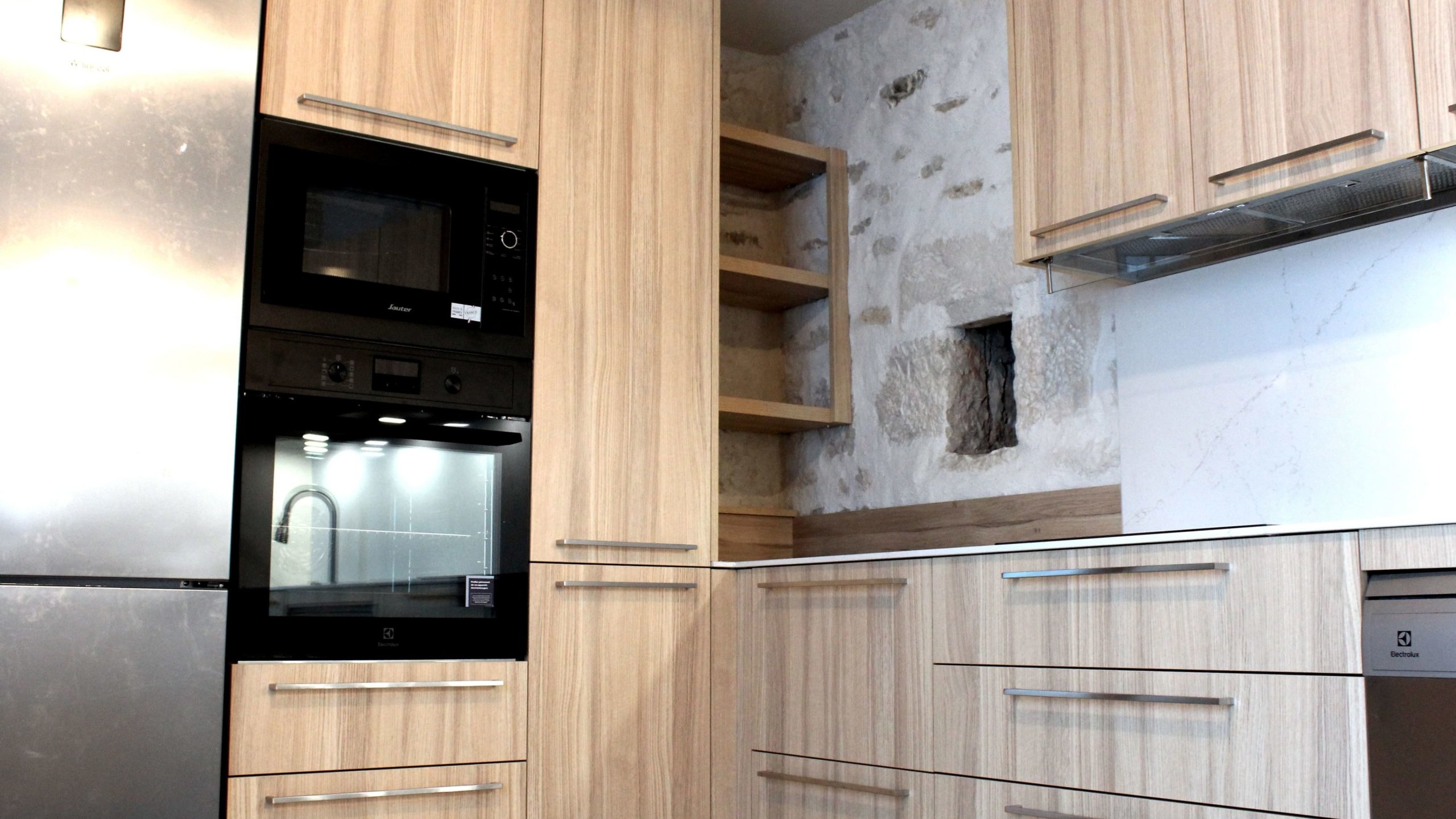 Cuisine moderne en placage bois clair avec plan de travail en quartz blanc, intégrée dans un intérieur en pierre à Nanteuil-en-Vallée.