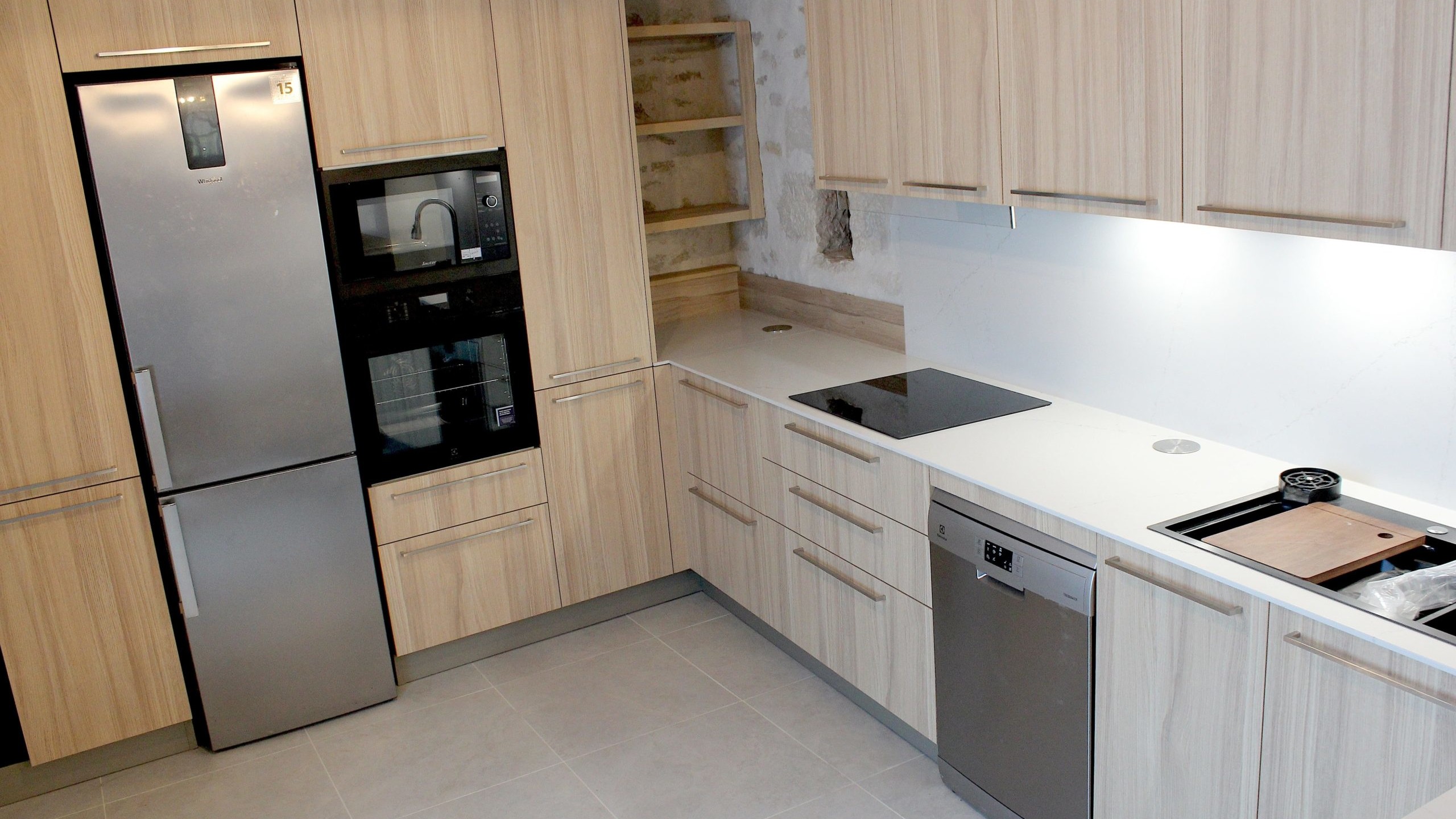 Cuisine moderne en placage bois clair avec plan de travail en quartz blanc, intégrée dans un intérieur en pierre à Nanteuil-en-Vallée.