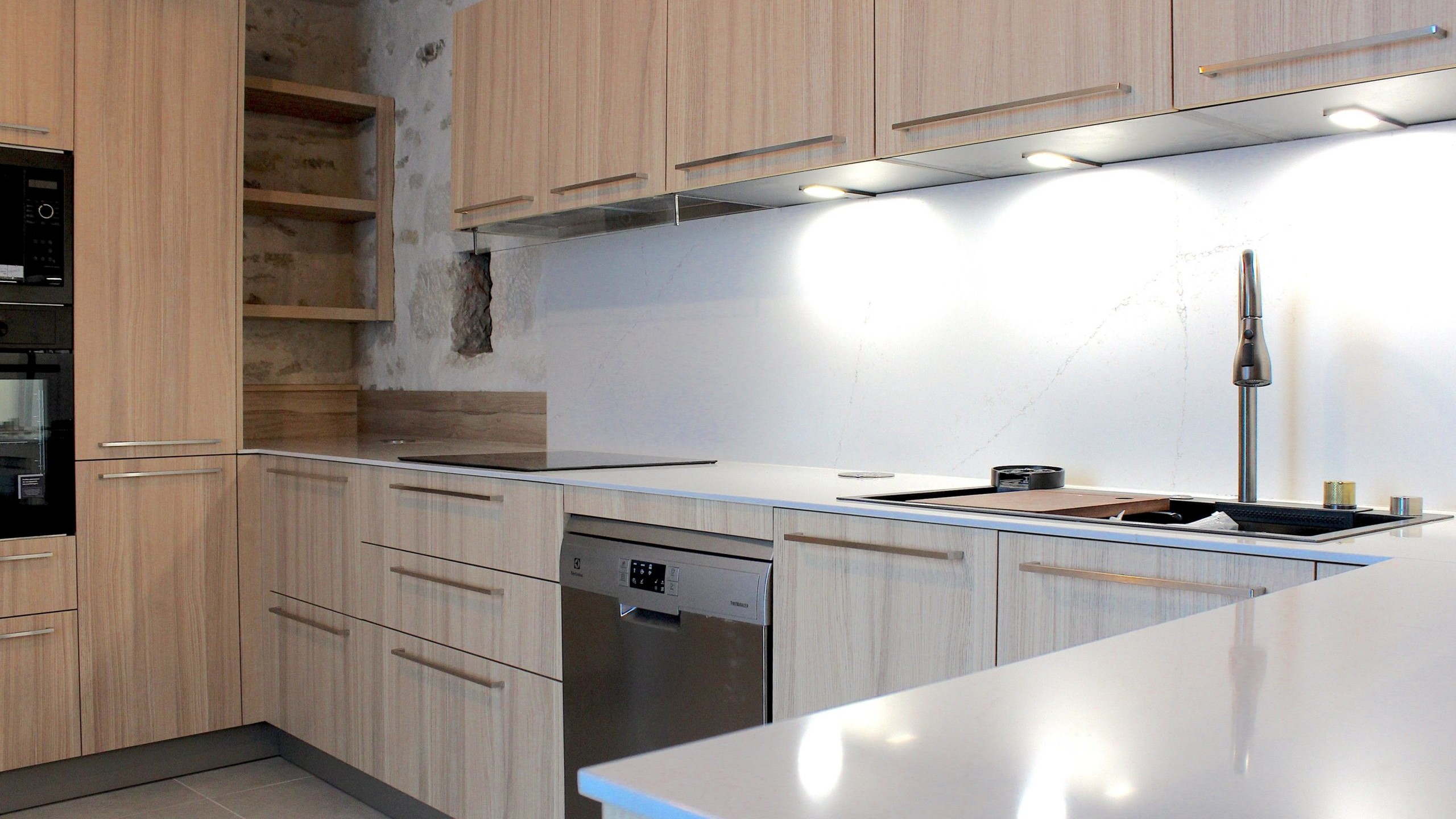 Cuisine moderne en placage bois clair avec plan de travail en quartz blanc, intégrée dans un intérieur en pierre à Nanteuil-en-Vallée.