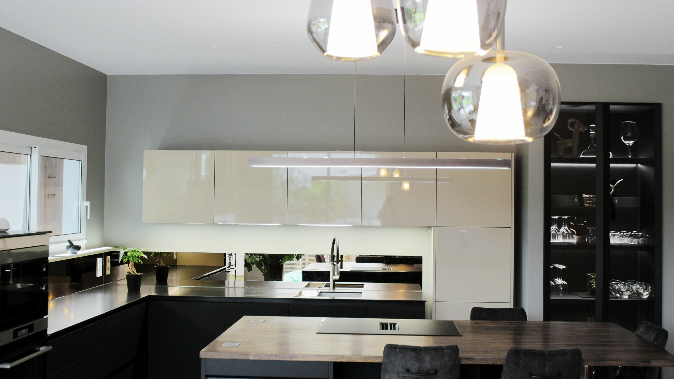 Cuisine moderne sur-mesure avec meubles Fenix noir mat, laque beige brillante, îlot central en bois wengé, plaque à induction avec hotte intégrée et crédence miroir bronze.