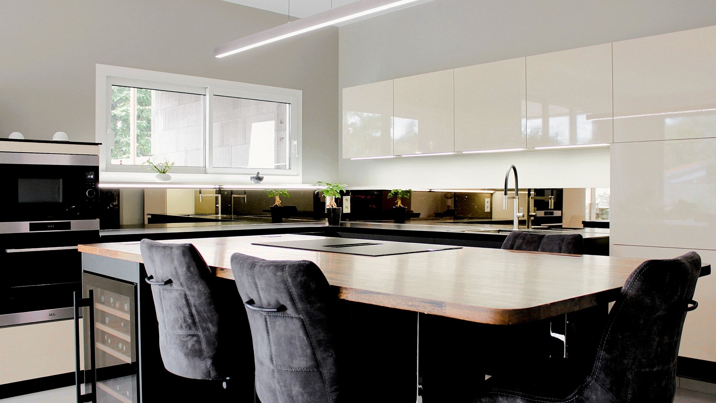 Cuisine moderne sur-mesure avec meubles Fenix noir mat, laque beige brillante, îlot central en bois wengé, plaque à induction avec hotte intégrée et crédence miroir bronze.