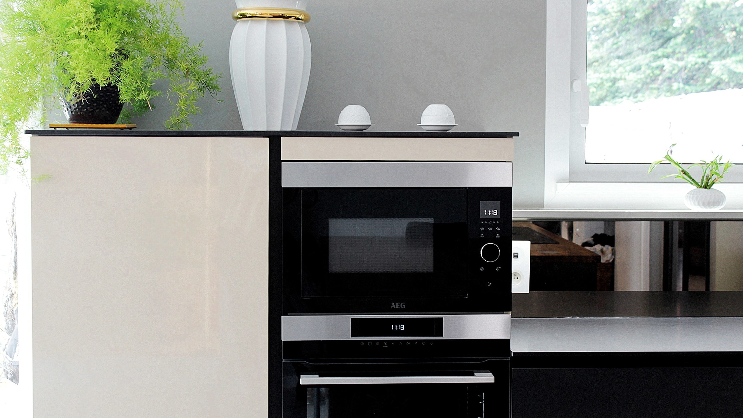 Cuisine moderne sur-mesure avec meubles Fenix noir mat, laque beige brillante, îlot central en bois wengé, plaque à induction avec hotte intégrée et crédence miroir bronze.