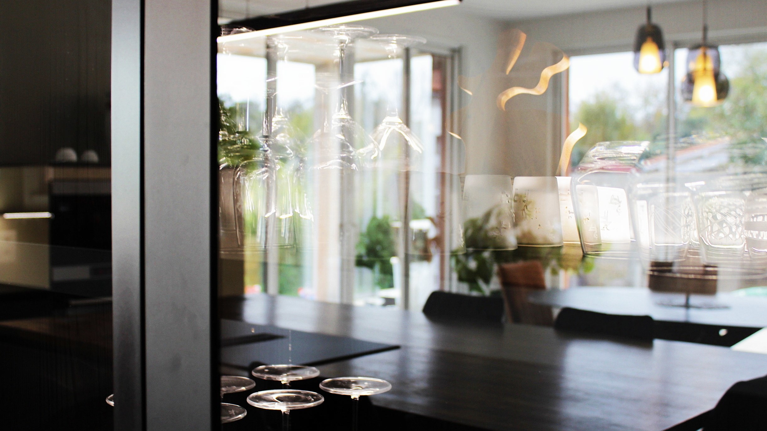 Cuisine moderne sur-mesure avec meubles Fenix noir mat, laque beige brillante, îlot central en bois wengé, plaque à induction avec hotte intégrée et crédence miroir bronze.