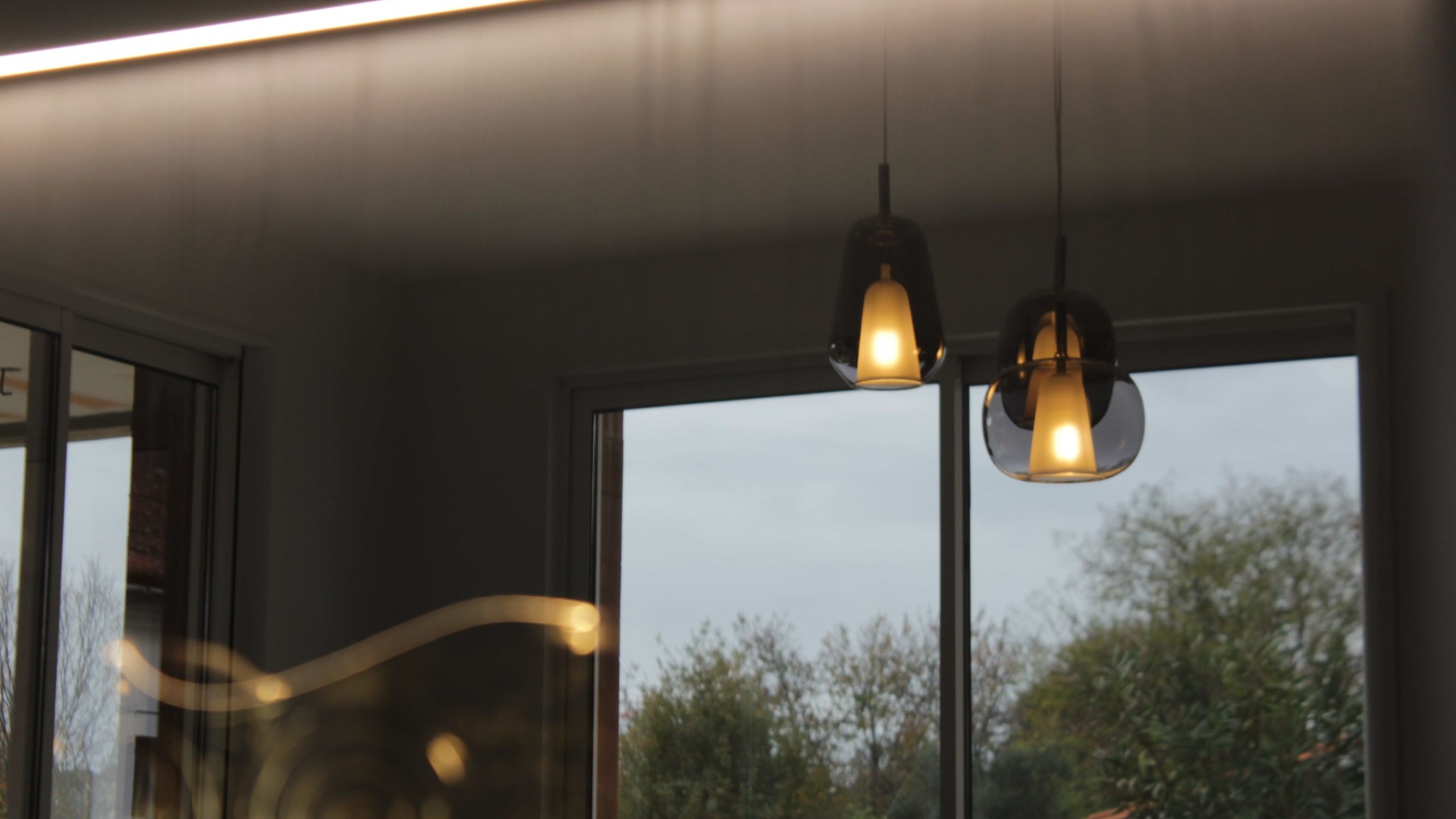 Cuisine moderne sur-mesure avec meubles Fenix noir mat, laque beige brillante, îlot central en bois wengé, plaque à induction avec hotte intégrée et crédence miroir bronze.