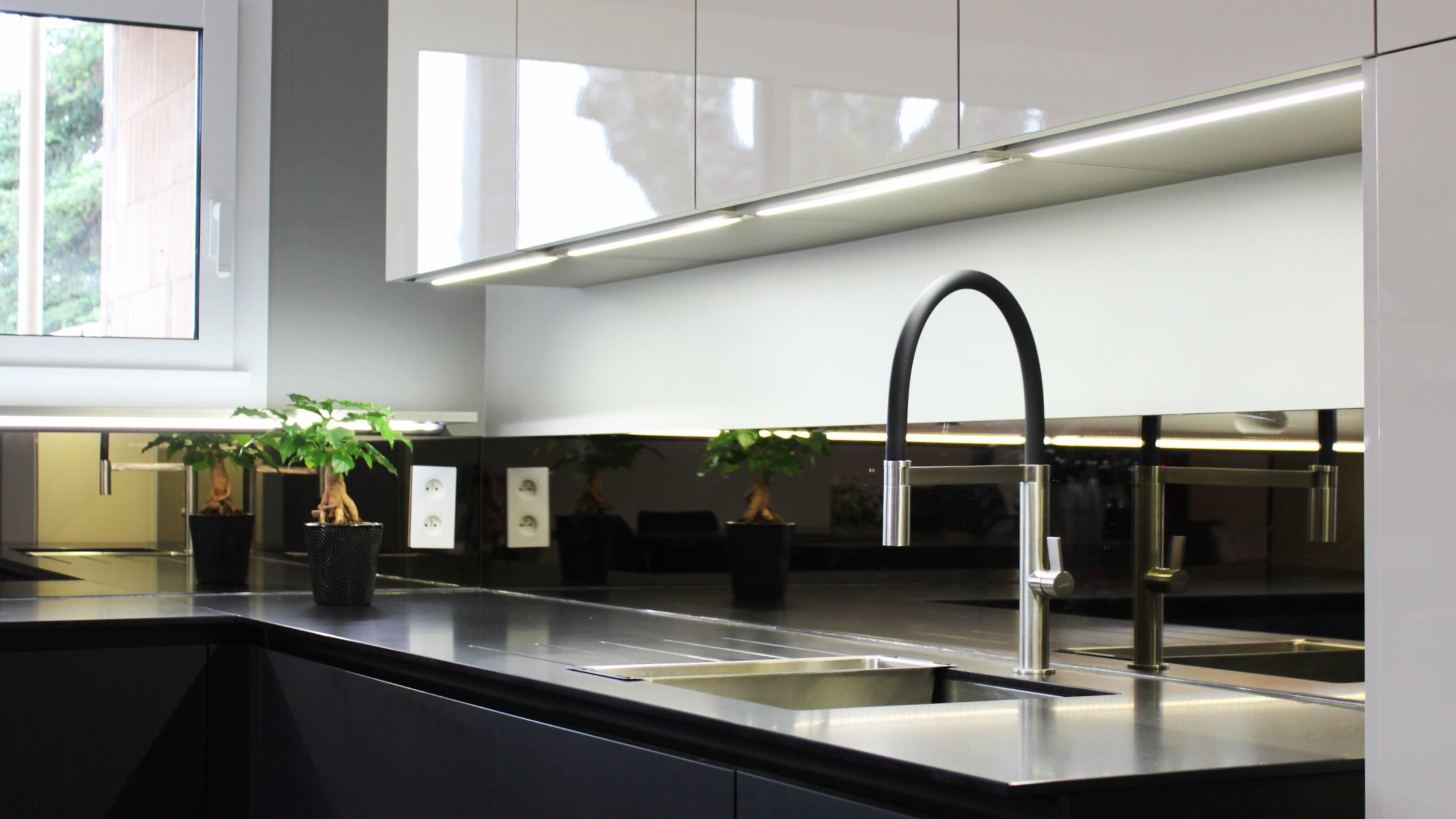 Cuisine moderne sur-mesure avec meubles Fenix noir mat, laque beige brillante, îlot central en bois wengé, plaque à induction avec hotte intégrée et crédence miroir bronze.