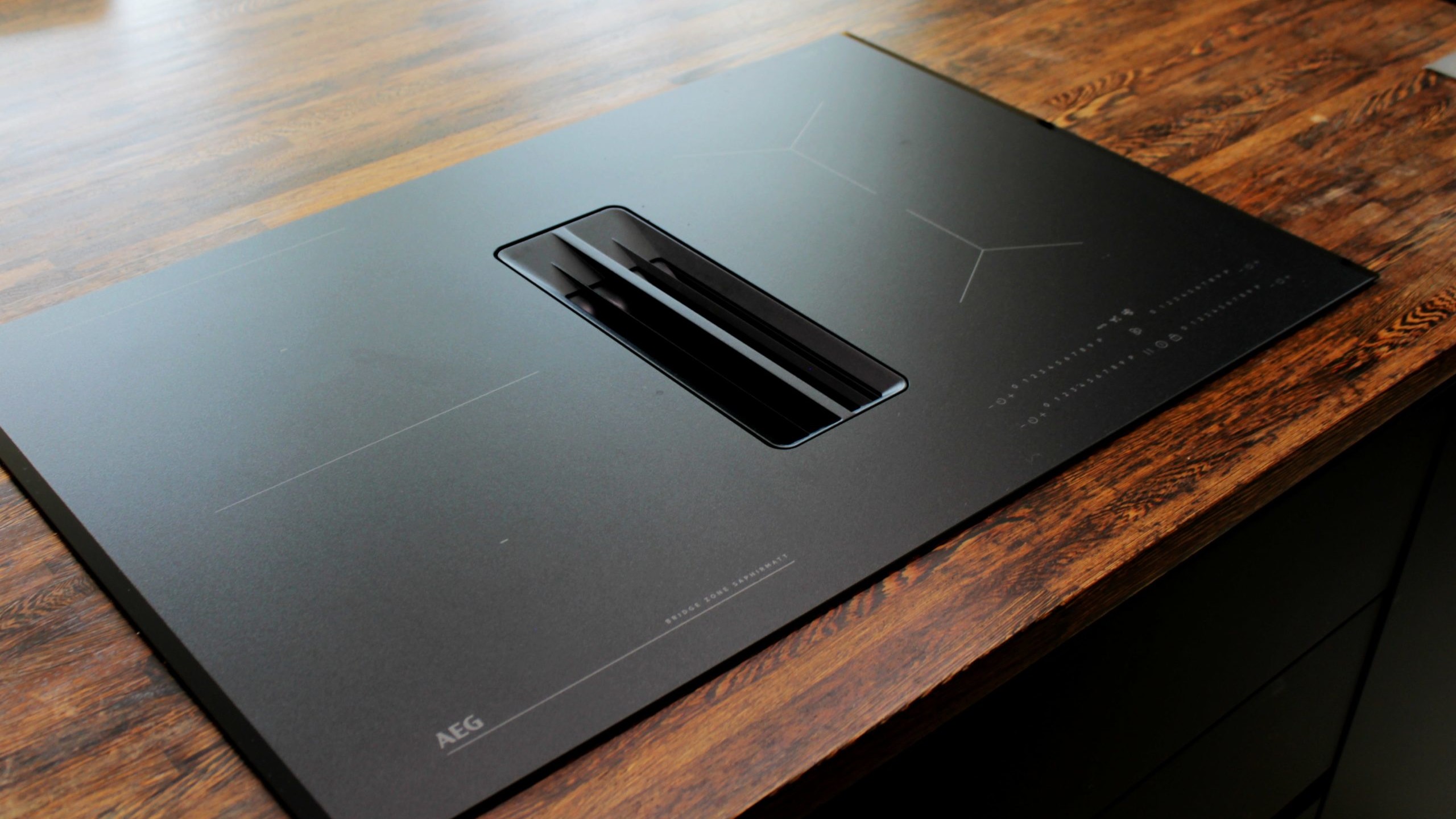 Cuisine moderne sur-mesure avec meubles Fenix noir mat, laque beige brillante, îlot central en bois wengé, plaque à induction avec hotte intégrée et crédence miroir bronze.