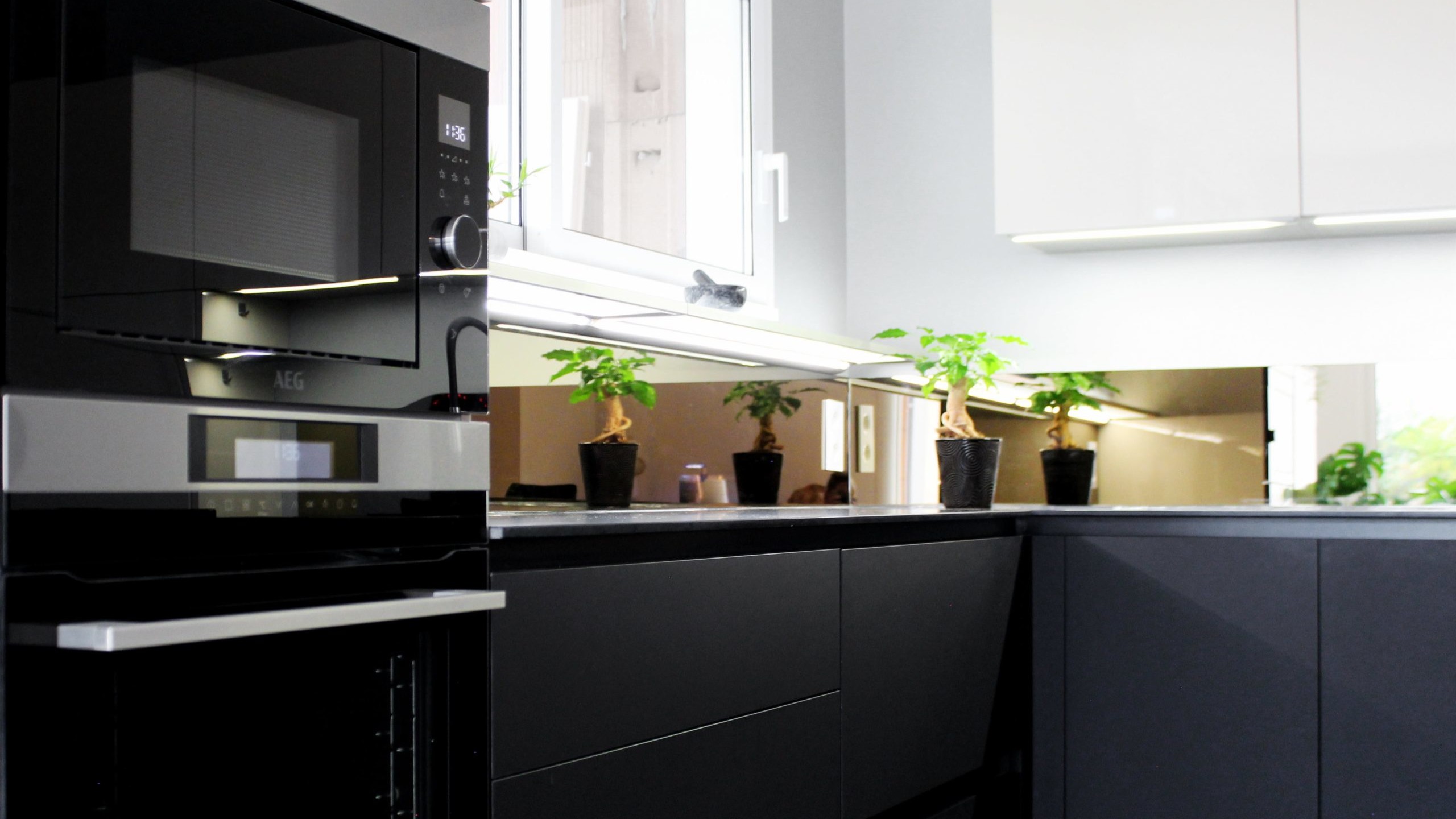 Cuisine moderne sur-mesure avec meubles Fenix noir mat, laque beige brillante, îlot central en bois wengé, plaque à induction avec hotte intégrée et crédence miroir bronze.