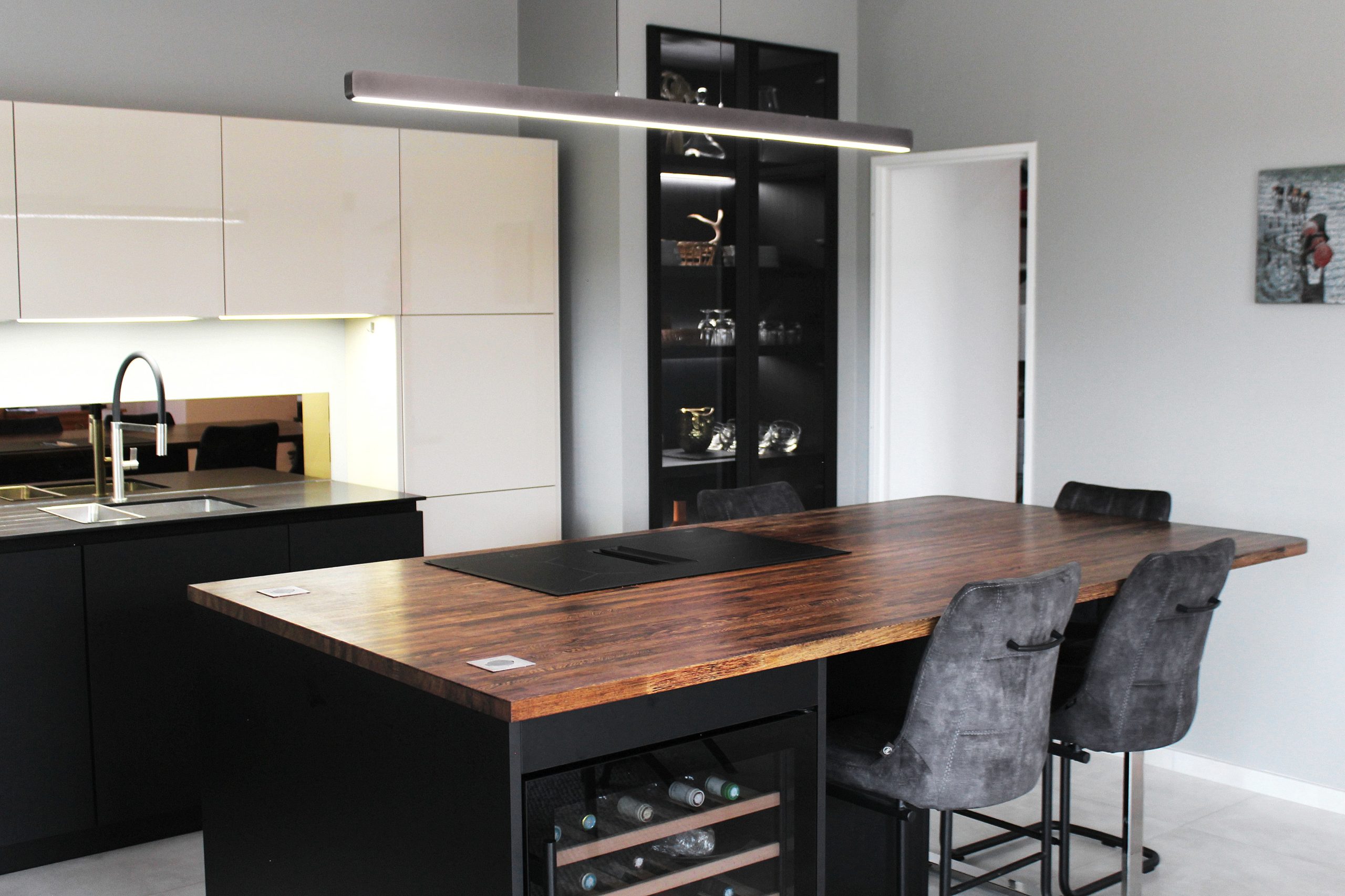 Cuisine moderne sur-mesure avec meubles Fenix noir mat, laque beige brillante, îlot central en bois wengé, plaque à induction avec hotte intégrée et crédence miroir bronze.