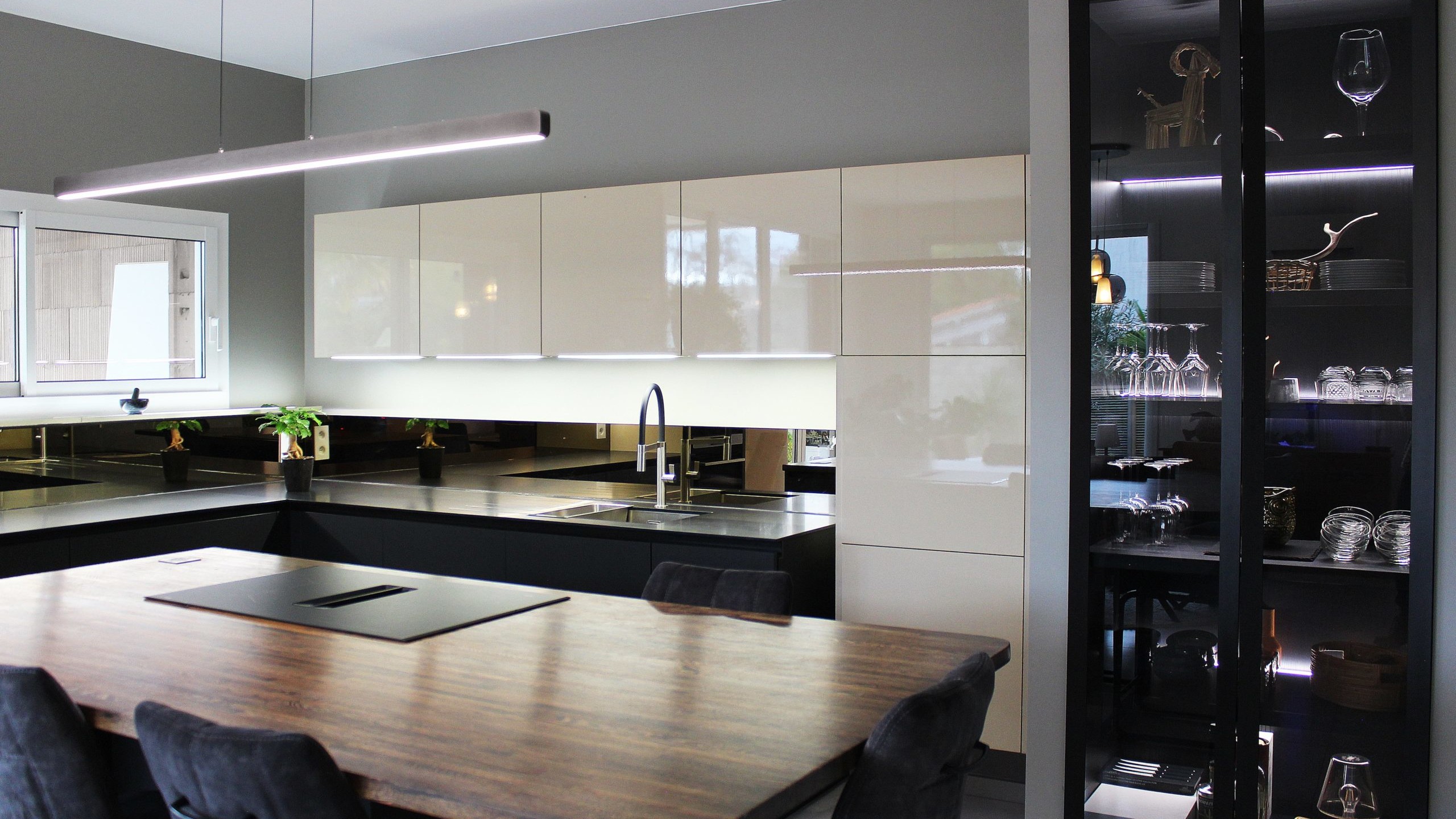 Cuisine moderne sur-mesure avec meubles Fenix noir mat, laque beige brillante, îlot central en bois wengé, plaque à induction avec hotte intégrée et crédence miroir bronze.