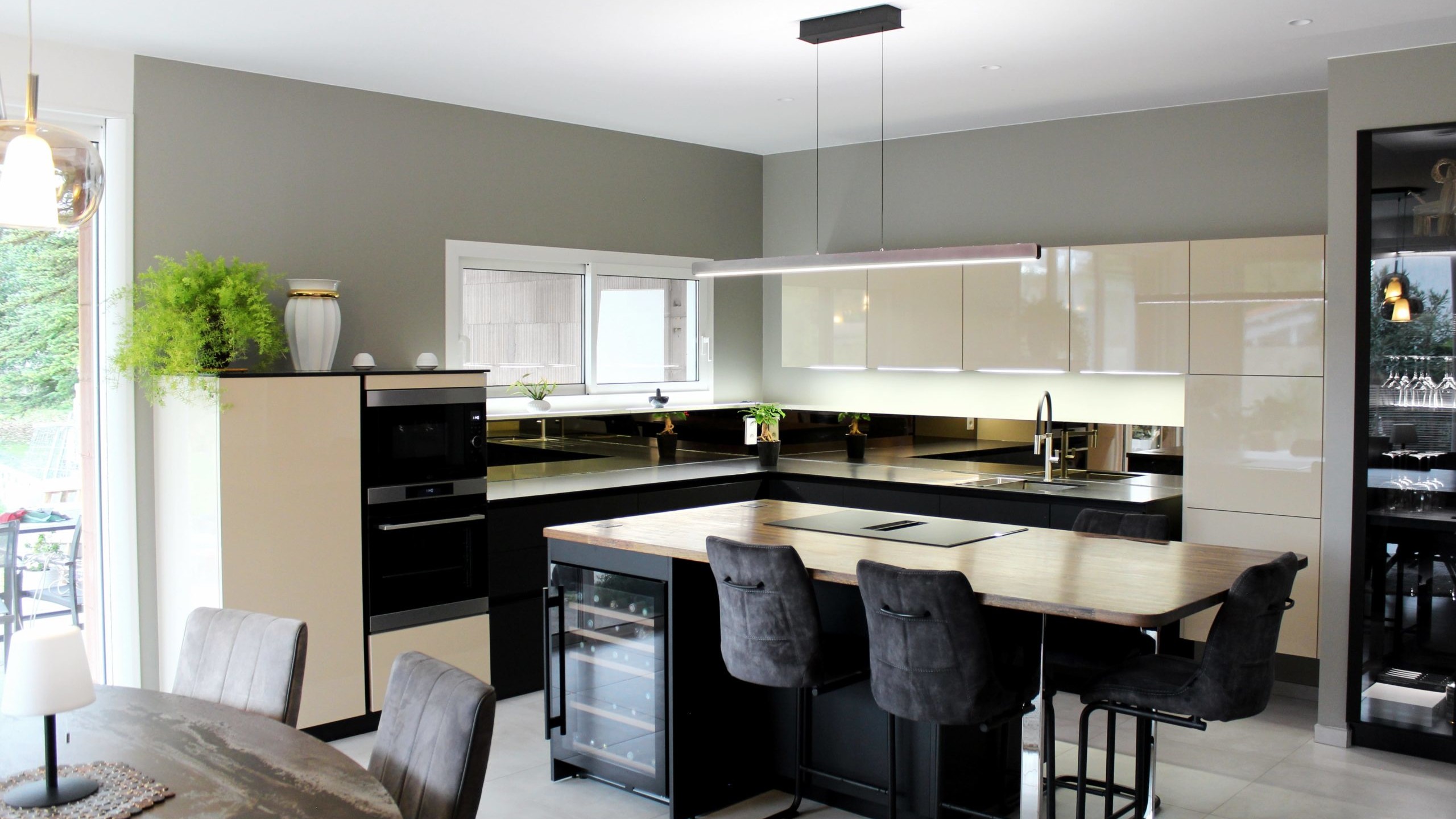 Cuisine moderne sur-mesure avec meubles Fenix noir mat, laque beige brillante, îlot central en bois wengé, plaque à induction avec hotte intégrée et crédence miroir bronze.