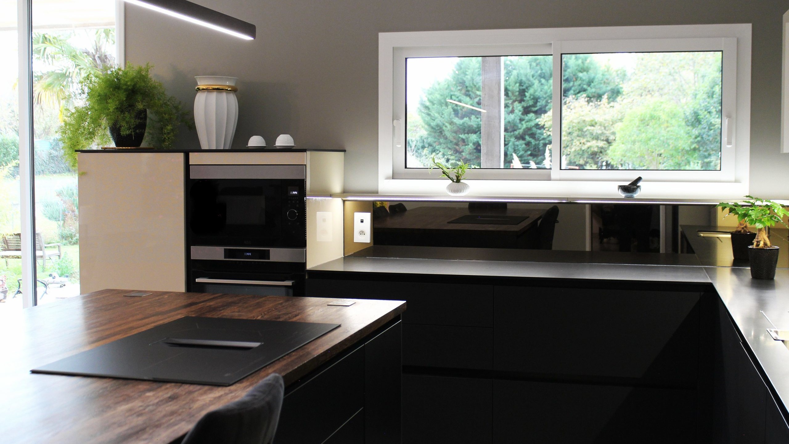 Cuisine moderne sur-mesure avec meubles Fenix noir mat, laque beige brillante, îlot central en bois wengé, plaque à induction avec hotte intégrée et crédence miroir bronze.