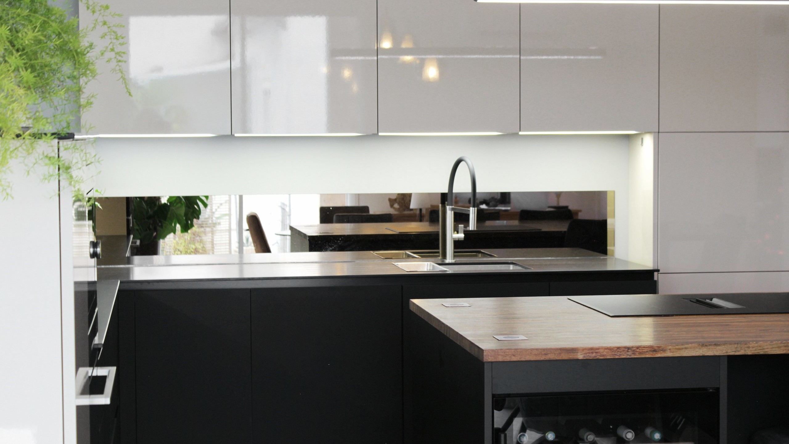 Cuisine moderne sur-mesure avec meubles Fenix noir mat, laque beige brillante, îlot central en bois wengé, plaque à induction avec hotte intégrée et crédence miroir bronze.