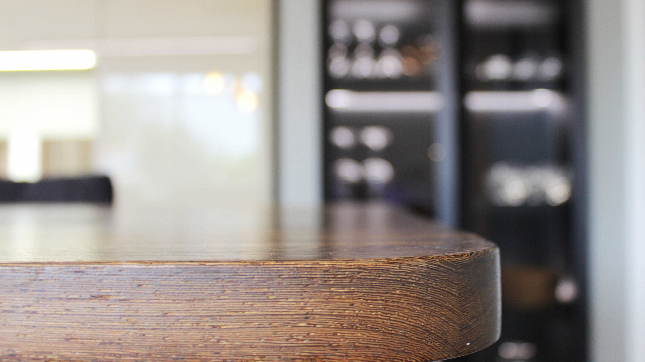 Cuisine moderne sur-mesure avec meubles Fenix noir mat, laque beige brillante, îlot central en bois wengé, plaque à induction avec hotte intégrée et crédence miroir bronze.