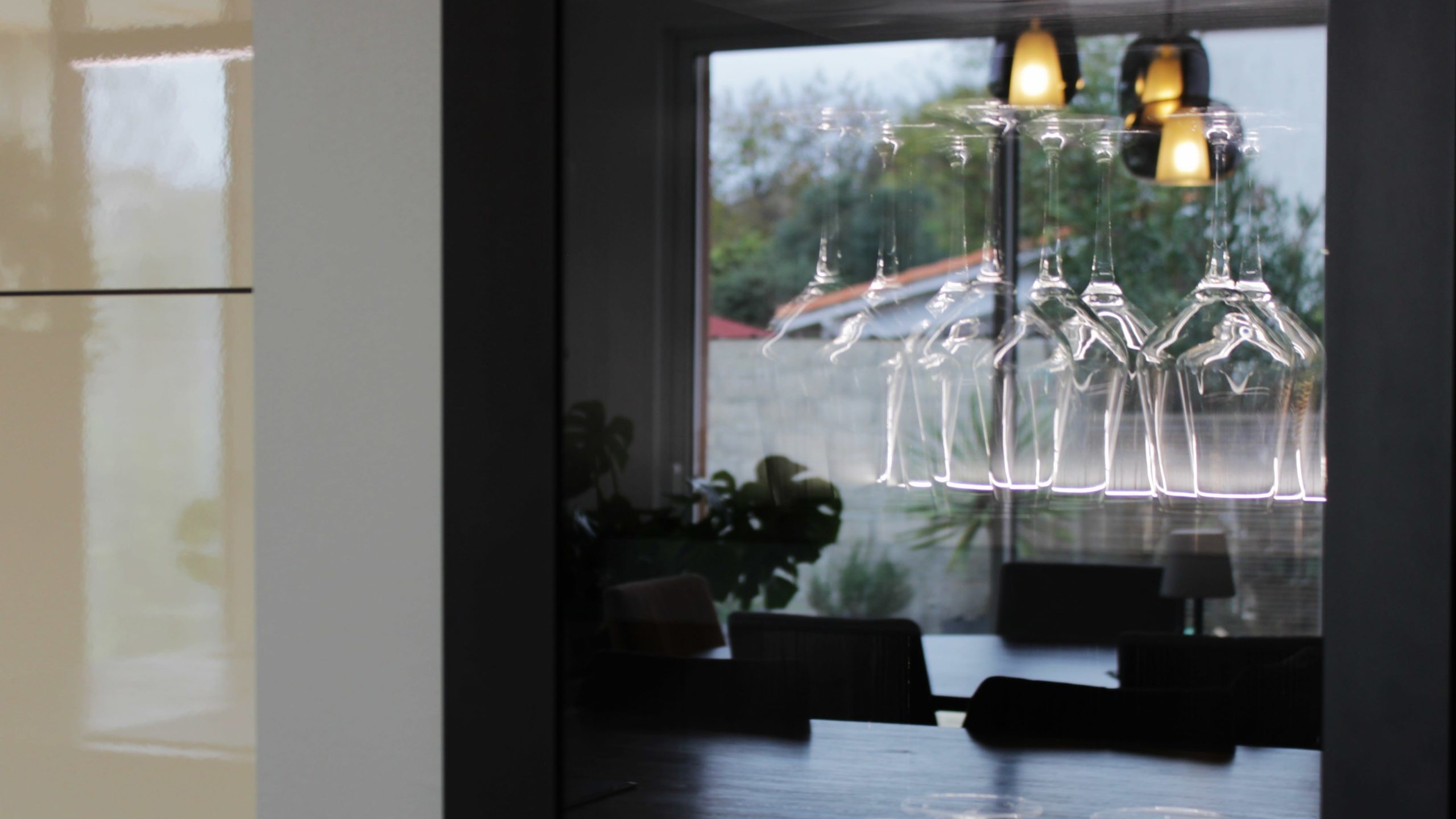 Cuisine moderne sur-mesure avec meubles Fenix noir mat, laque beige brillante, îlot central en bois wengé, plaque à induction avec hotte intégrée et crédence miroir bronze.