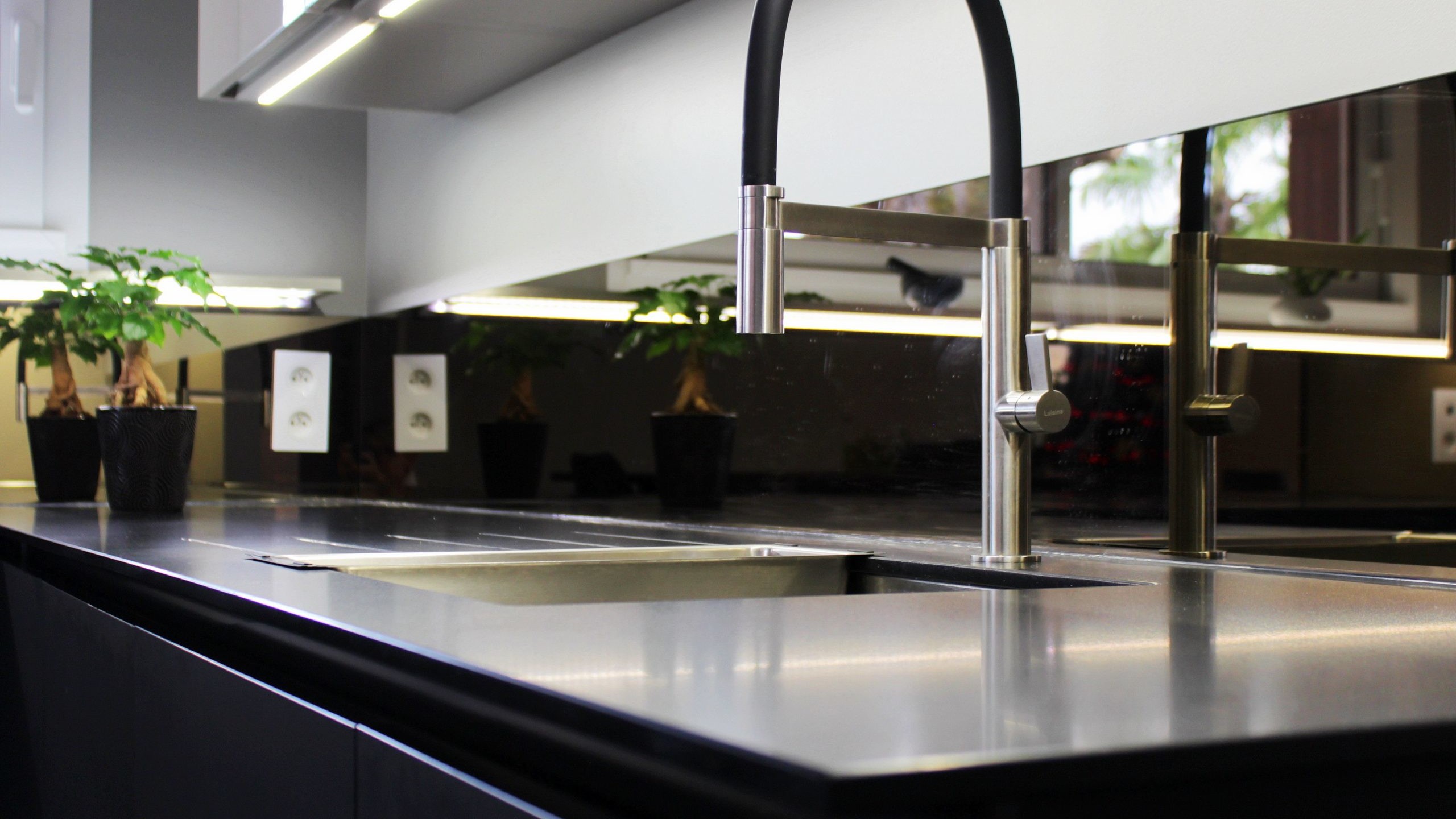 Cuisine moderne sur-mesure avec meubles Fenix noir mat, laque beige brillante, îlot central en bois wengé, plaque à induction avec hotte intégrée et crédence miroir bronze.