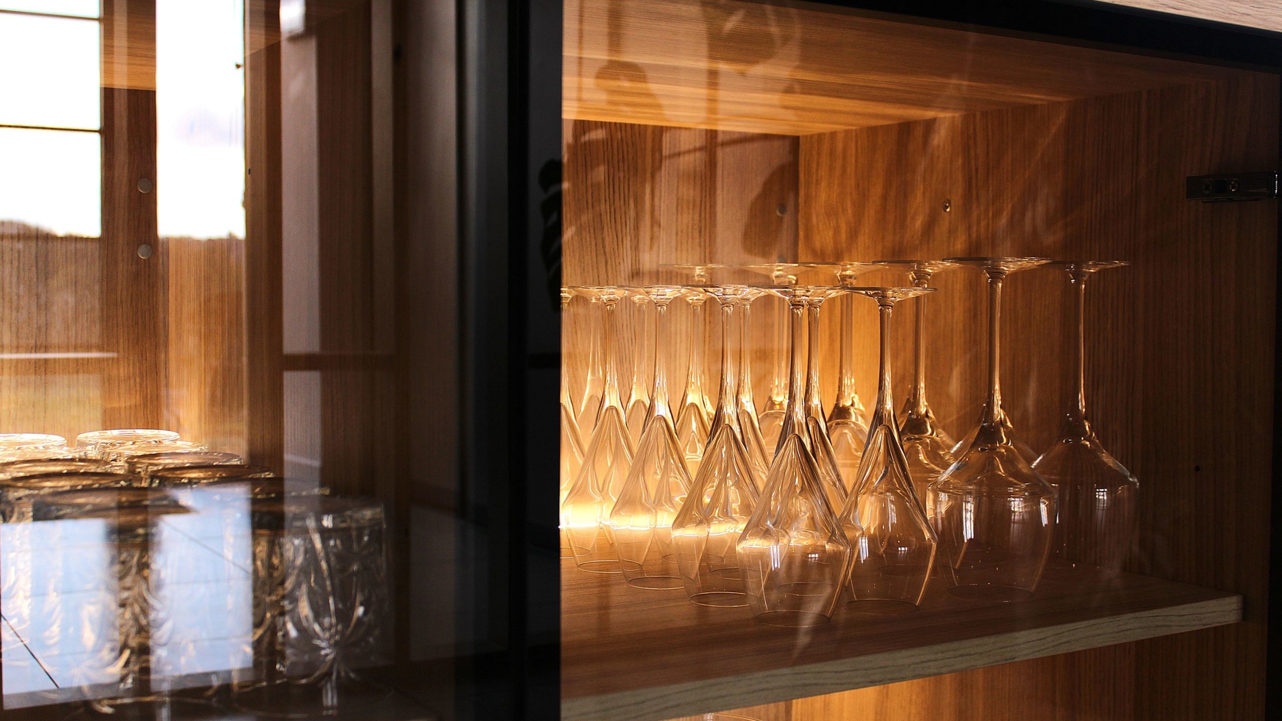 Cette cuisine contemporaine a été pensée comme un véritable espace de vie, alliant esthétique minimaliste, matériaux naturels et fonctionnalité au quotidien. L’association du bois clair et des façades blanches sans poignées apporte une sensation immédiate de luminosité et de sérénité. Au cœur de la pièce, l’îlot central s’impose comme un élément structurant. Il intègre une plaque de cuisson discrète, de nombreux rangements et une grande table en bois massif, idéale pour partager les repas, travailler ou recevoir. Cet aménagement favorise la convivialité tout en conservant une circulation fluide dans l’espace. La poutre en bois apparente traverse la pièce et lui confère un caractère unique, créant un dialogue harmonieux entre architecture traditionnelle et design contemporain. L’éclairage suspendu, aux lignes sobres et graphiques, souligne l’îlot et apporte une touche moderne élégante. Les espaces de rangement intégrés, l’électroménager encastré et les finitions soignées participent à une lecture visuelle épurée. Les touches végétales viennent parfaire l’ensemble en apportant fraîcheur et naturel. Pensée dans les moindres détails, cette cuisine offre un cadre à la fois chaleureux, fonctionnel et durable, parfaitement adapté à un art de vivre moderne.