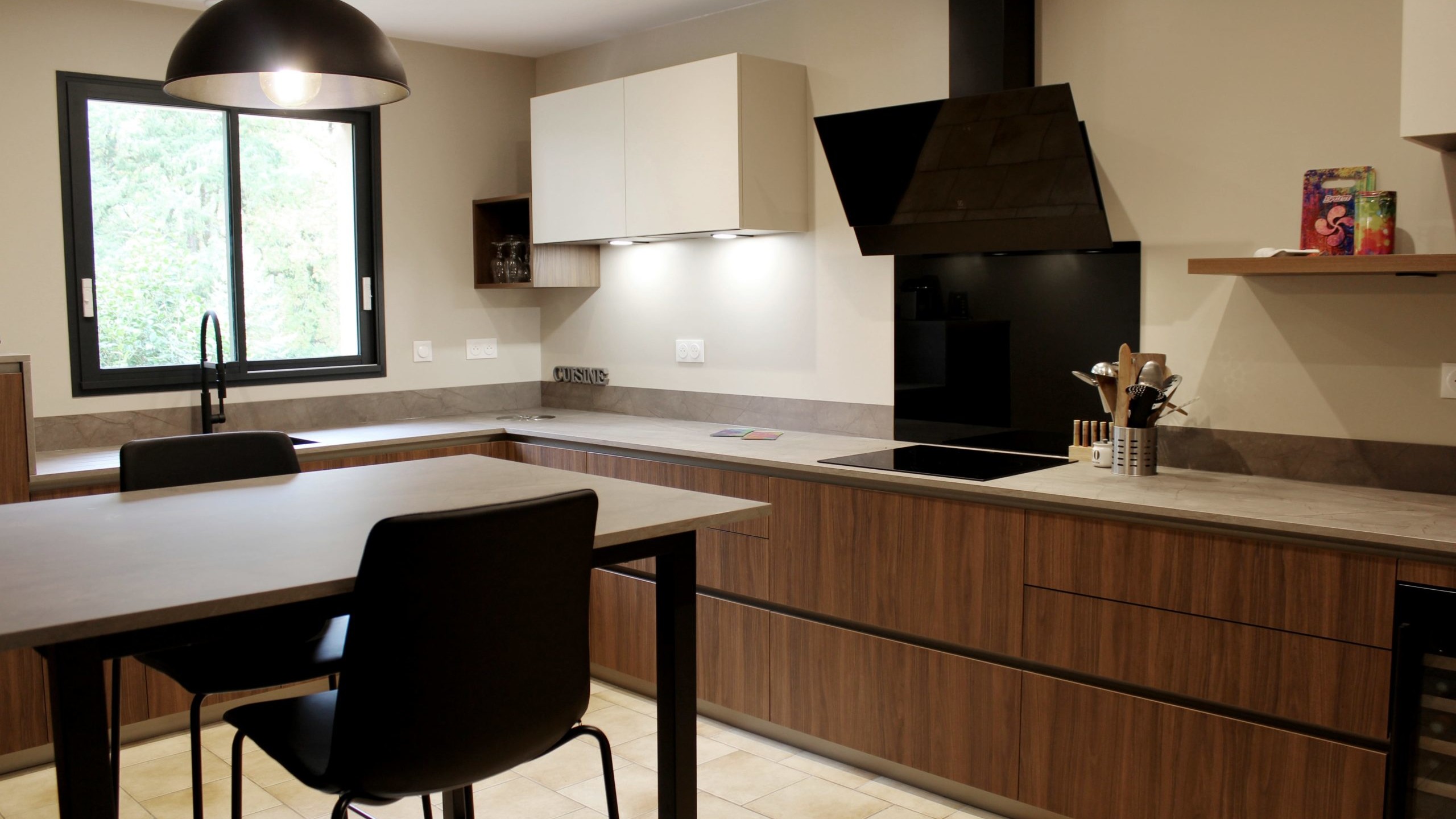 Cuisine moderne en noyer avec meubles clairs, hotte noire, éclairage discret et détails dorés subtils.