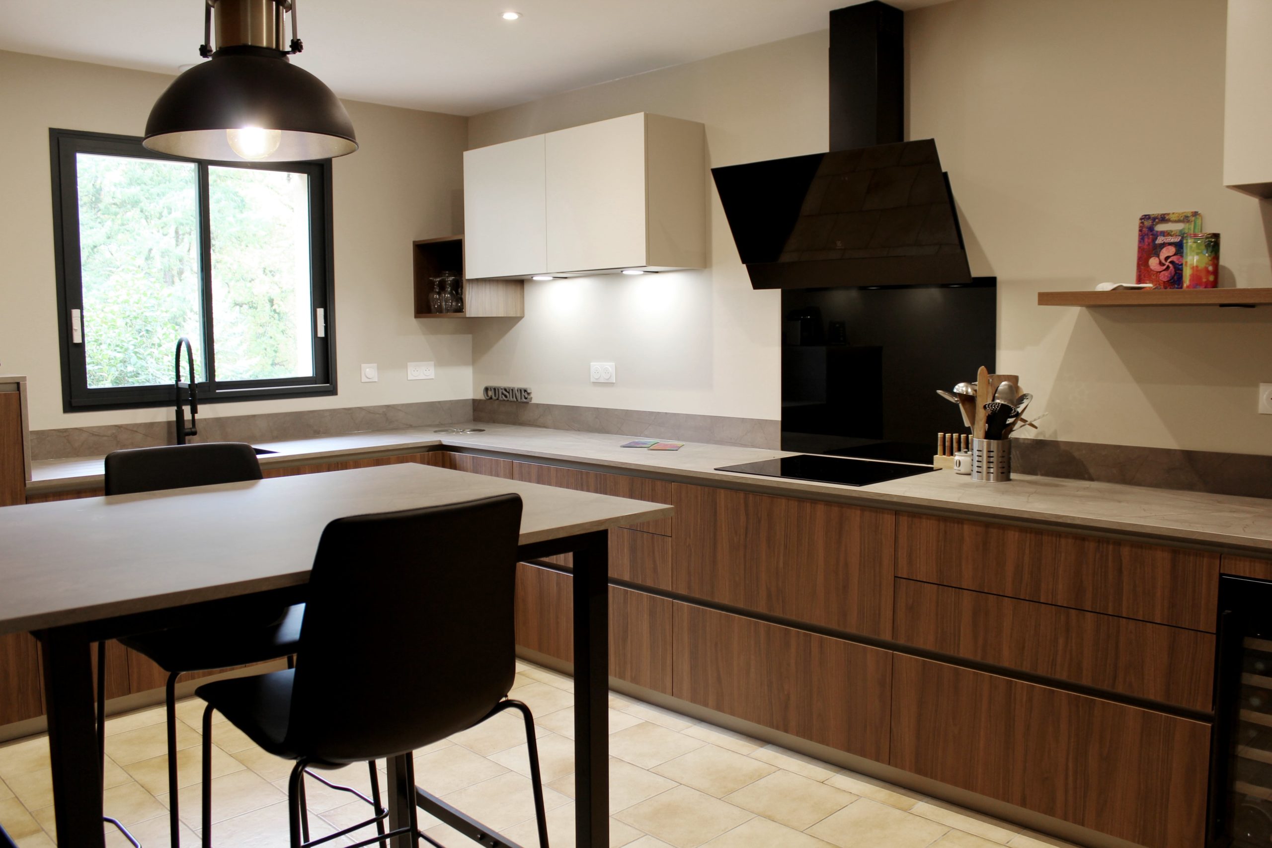 Cuisine moderne en noyer avec meubles clairs, hotte noire, éclairage discret et détails dorés subtils.