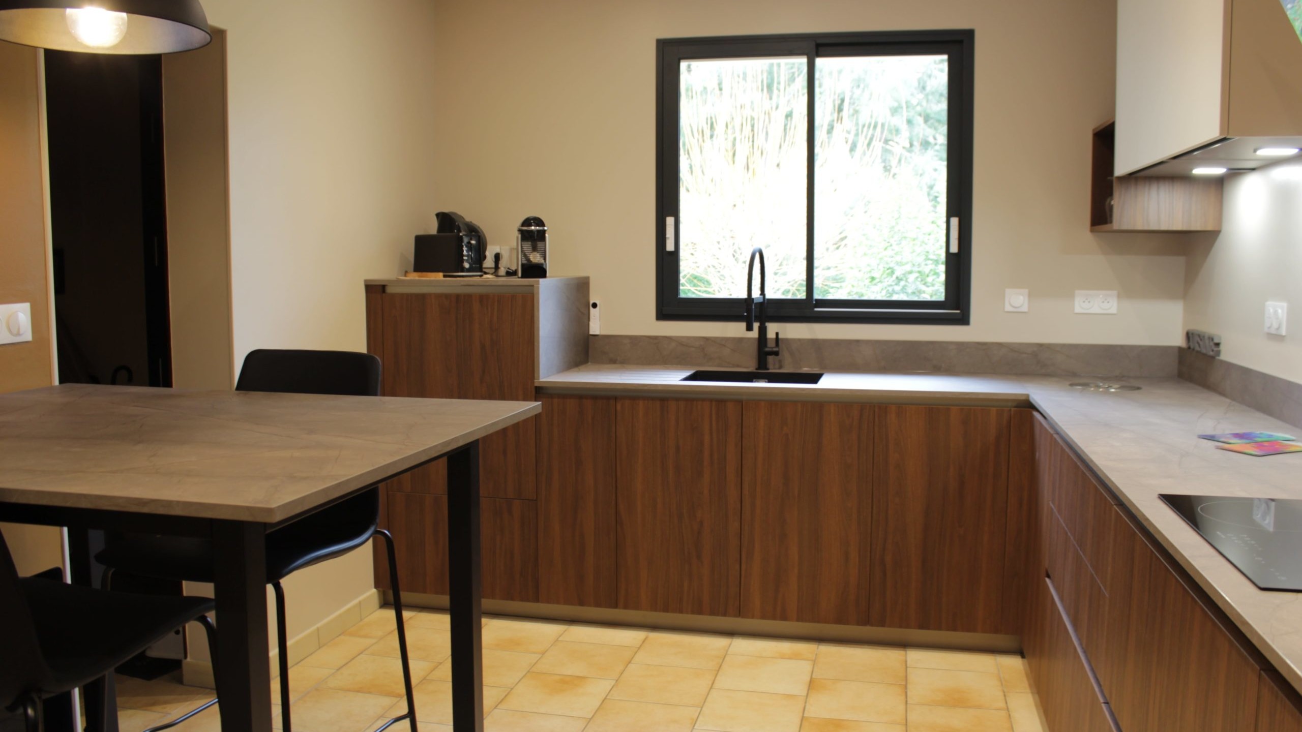 Cuisine moderne en noyer avec meubles clairs, hotte noire, éclairage discret et détails dorés subtils.