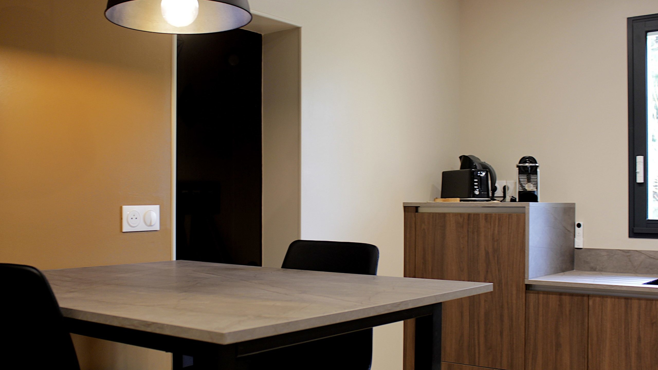 Cuisine moderne en noyer avec meubles clairs, hotte noire, éclairage discret et détails dorés subtils.