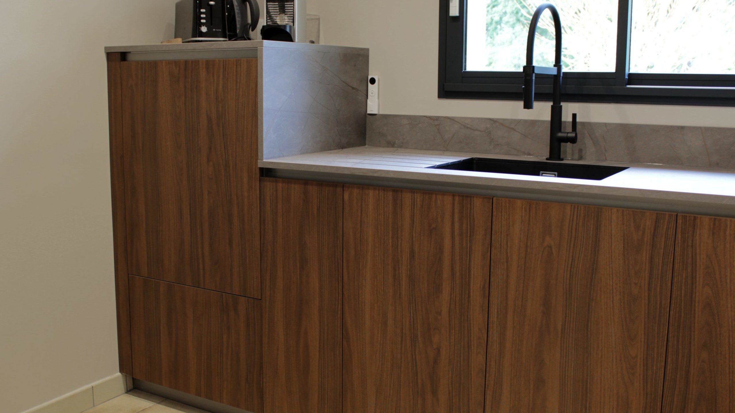 Cuisine moderne en noyer avec meubles clairs, hotte noire, éclairage discret et détails dorés subtils.