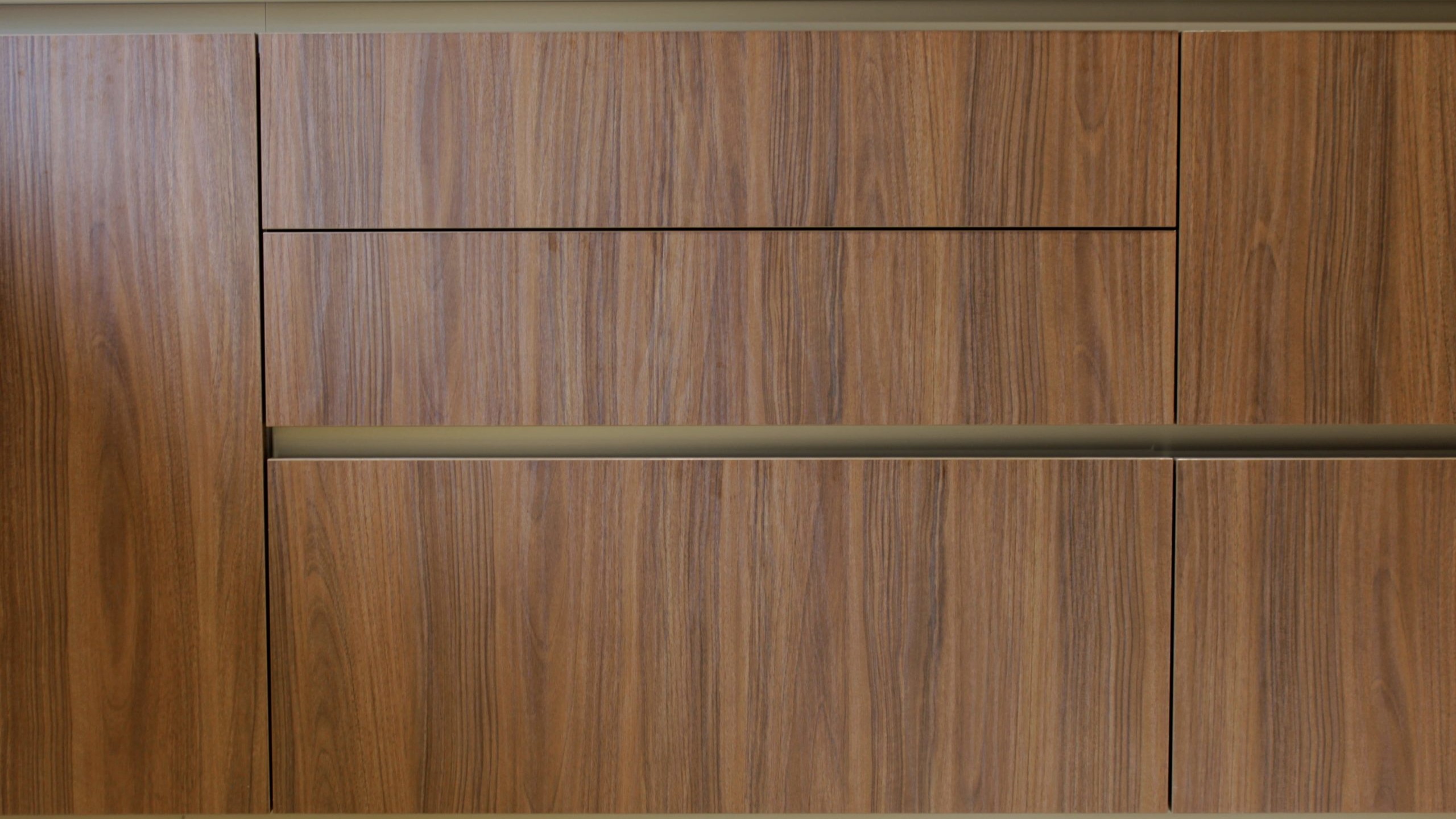 Cuisine moderne en noyer avec meubles clairs, hotte noire, éclairage discret et détails dorés subtils.