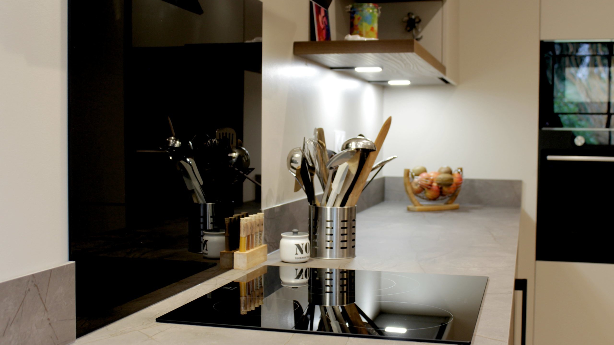 Cuisine moderne en noyer avec meubles clairs, hotte noire, éclairage discret et détails dorés subtils.