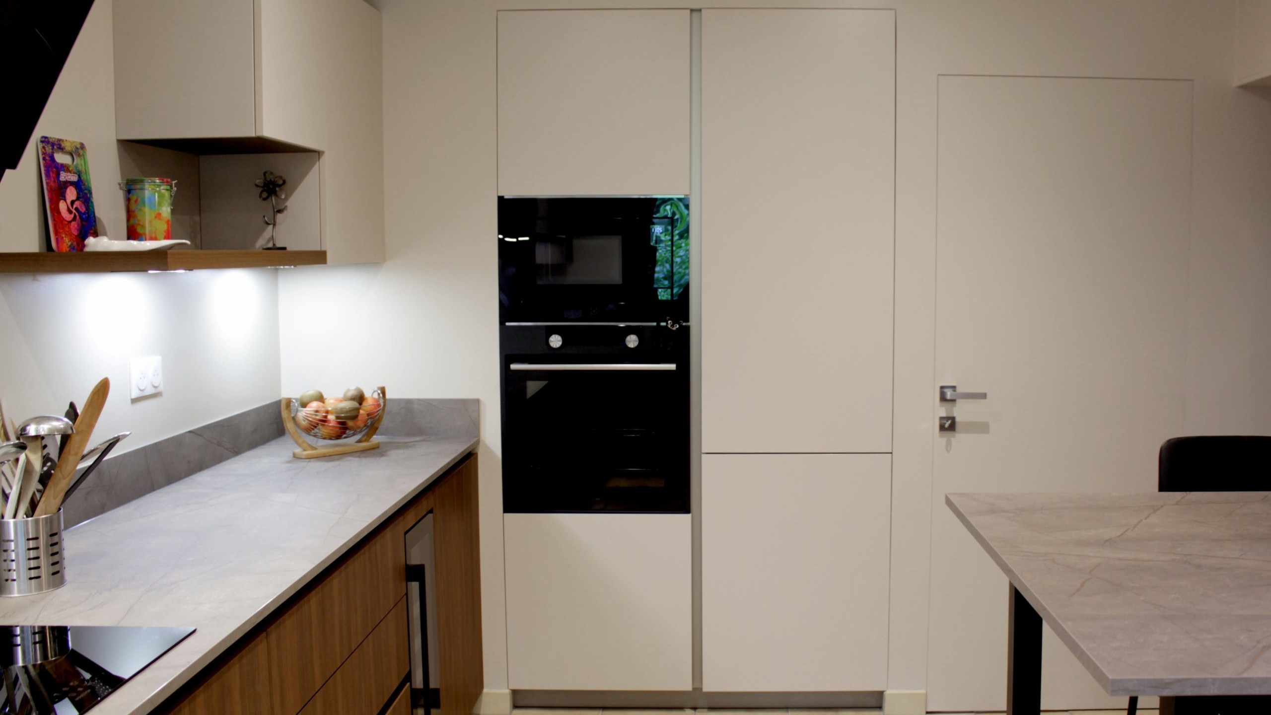 Cuisine moderne en noyer avec meubles clairs, hotte noire, éclairage discret et détails dorés subtils.