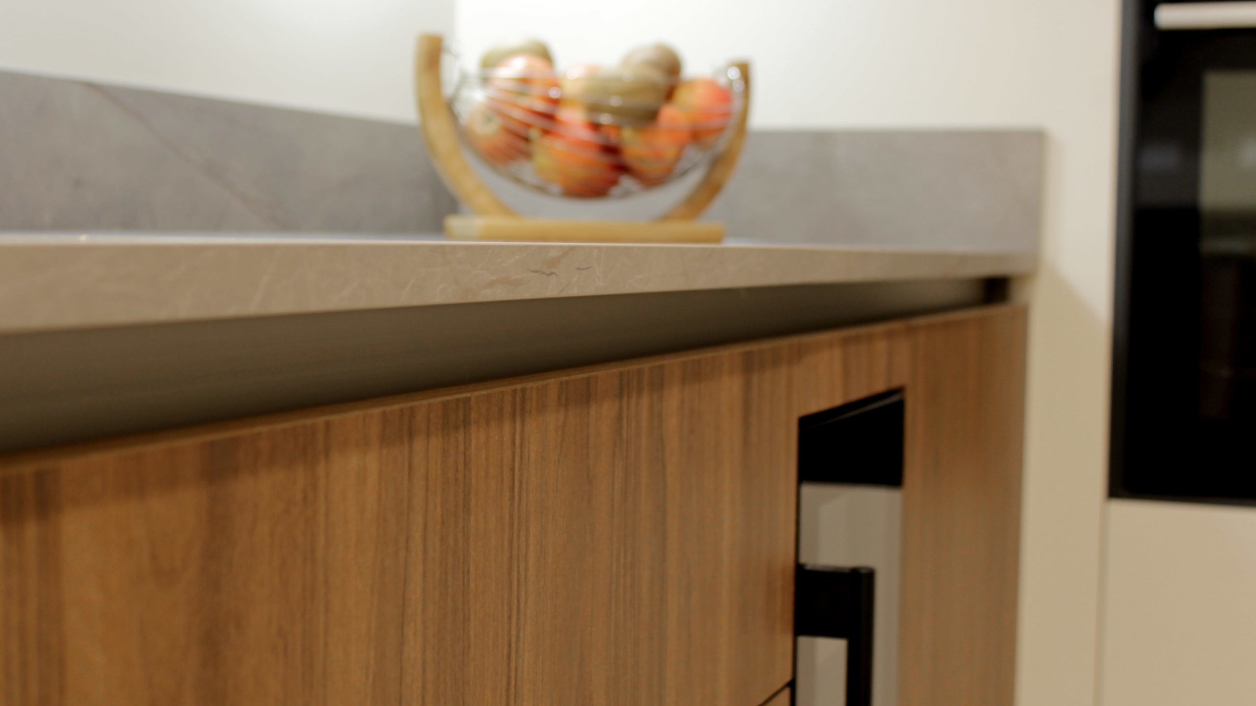 Cuisine moderne en noyer avec meubles clairs, hotte noire, éclairage discret et détails dorés subtils.