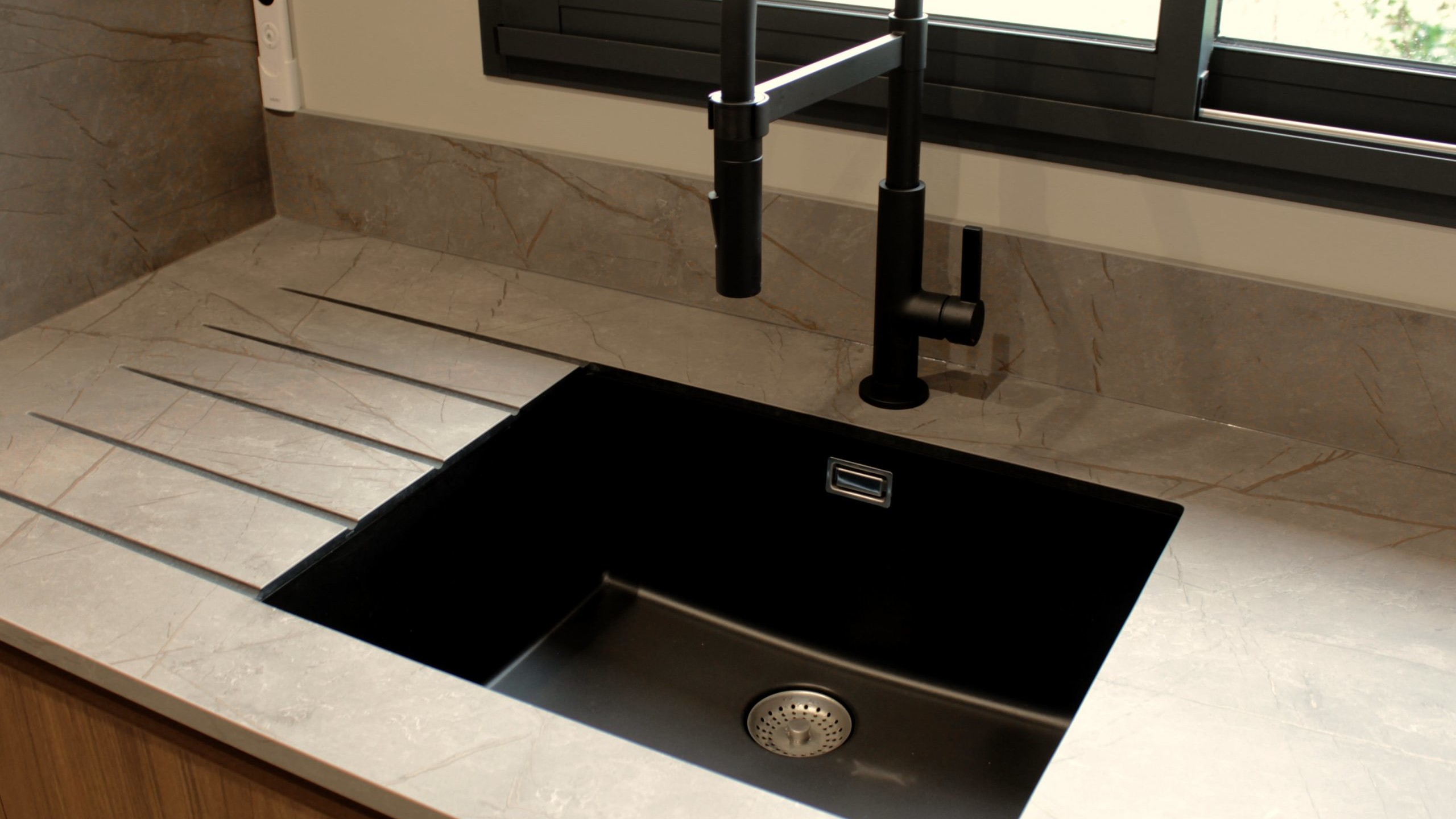 Cuisine moderne en noyer avec meubles clairs, hotte noire, éclairage discret et détails dorés subtils.